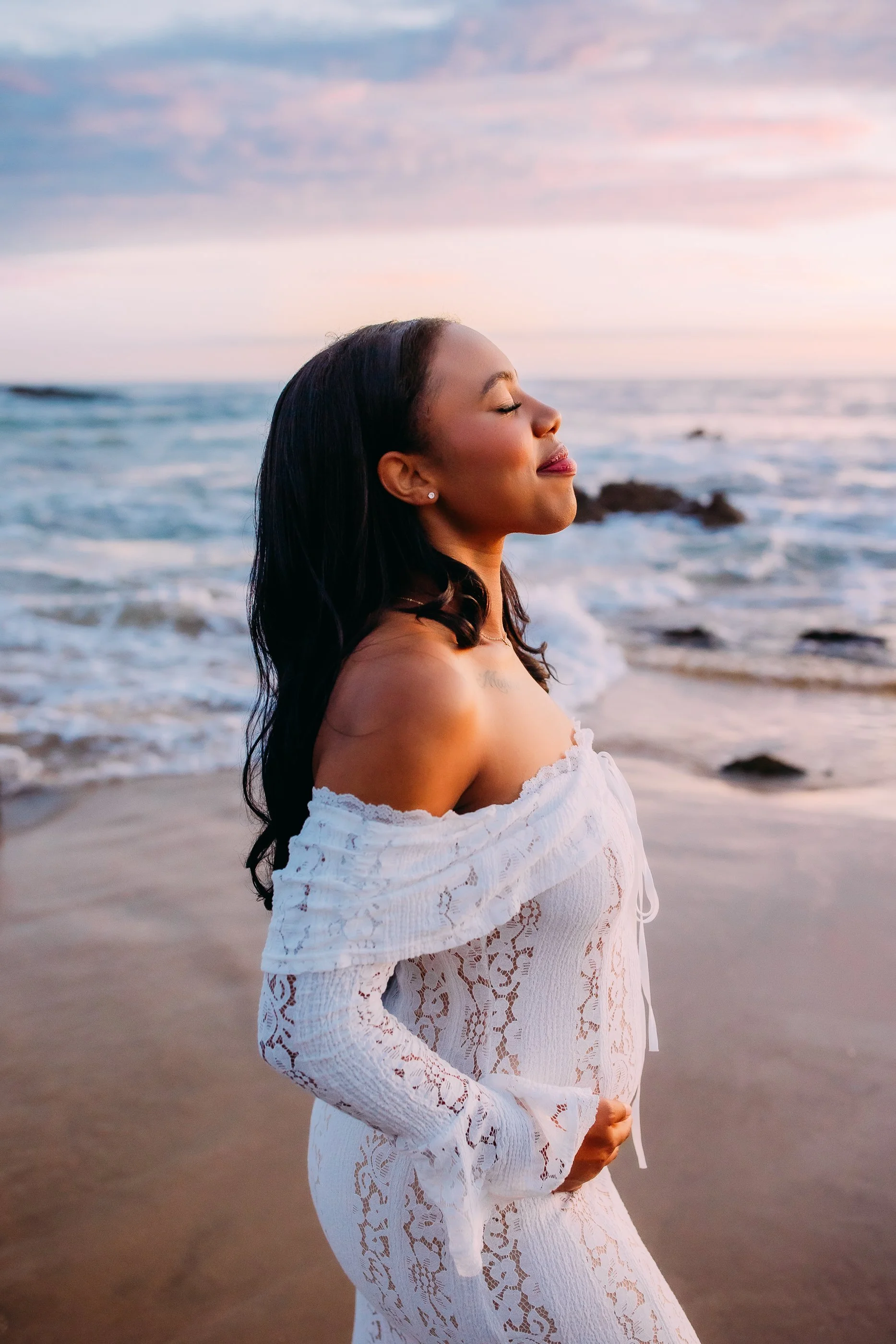 mom to be softly smiling out towards the ocean during her pregnancy announcement photoshoot in Newport Beach, California