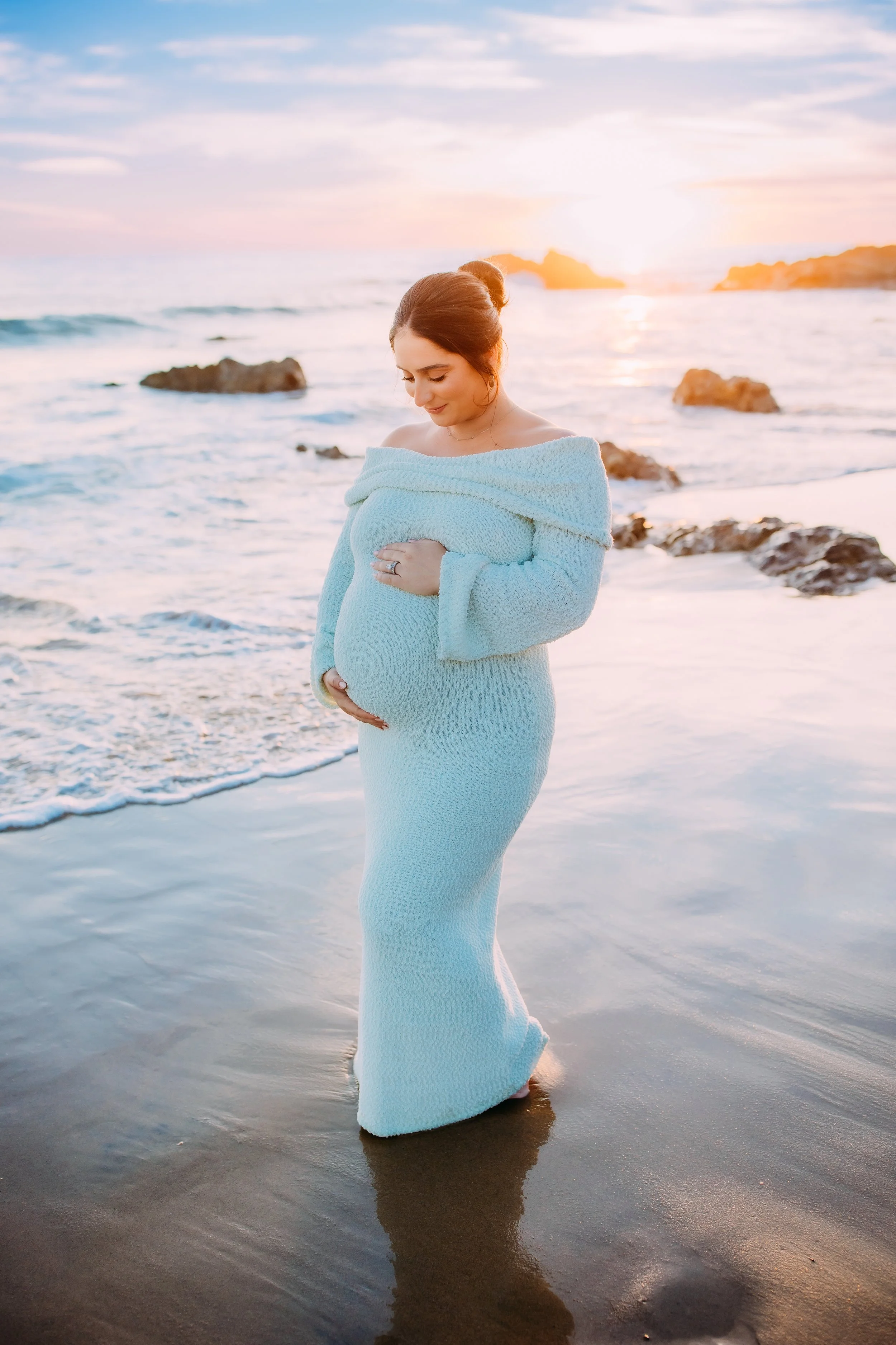 mom to be gazing down at her belly during her sunset photoshoot in Newport Beach, California