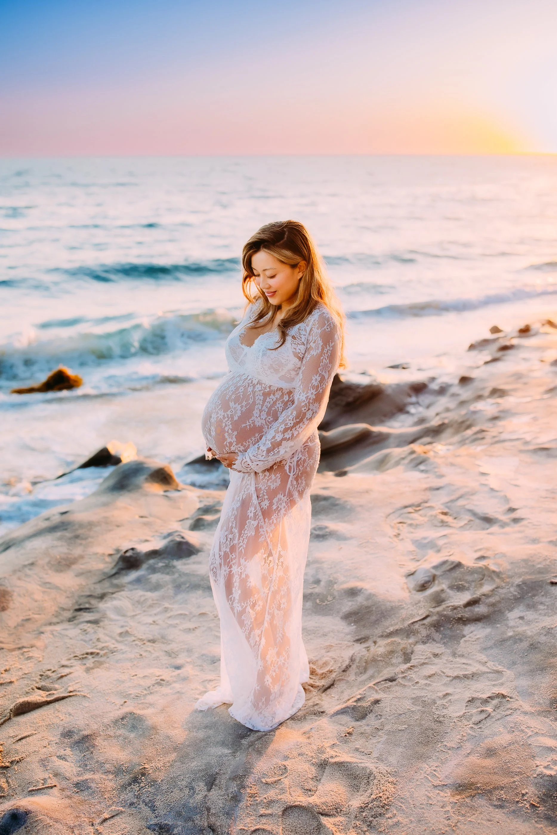 mom to be holding her belly while smiling during her sunset photoshoot in Laguna Beach, California