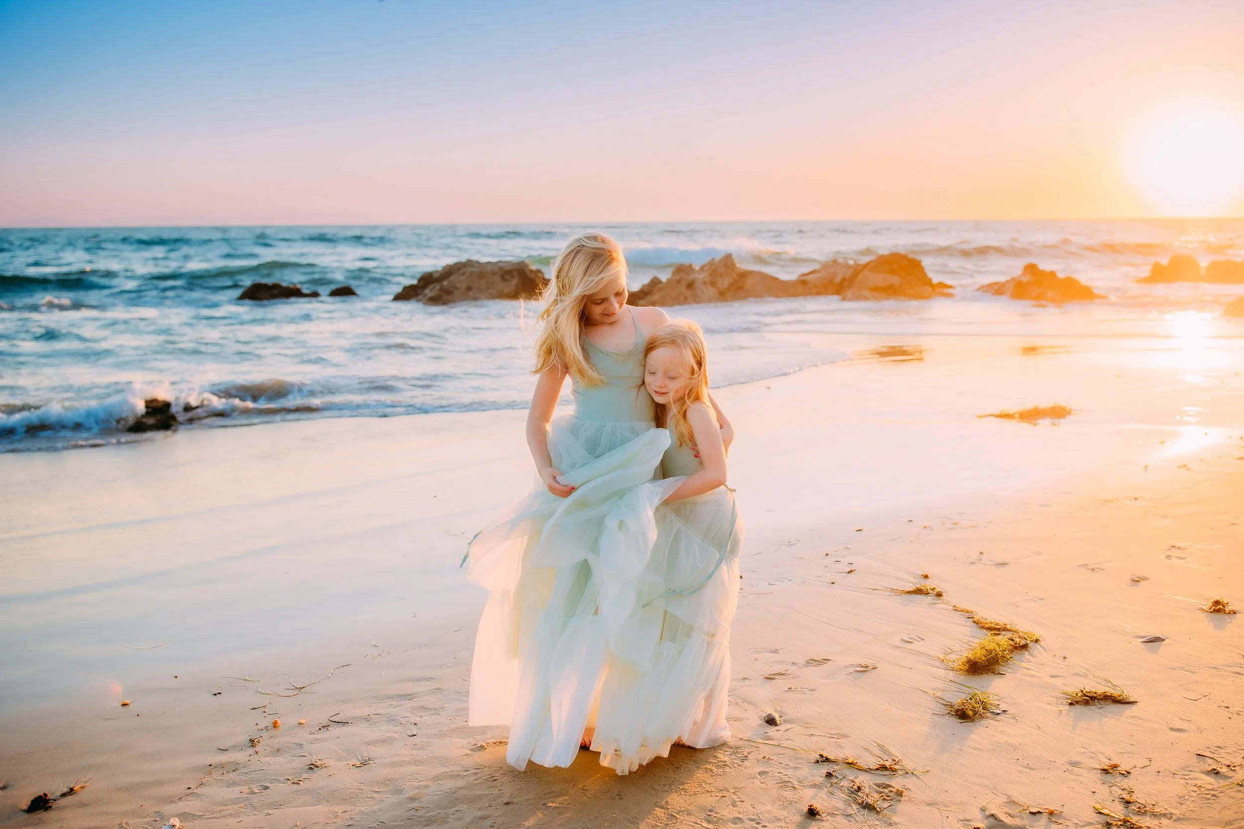sisters embracing while their hair and dresses blow in the wind during their family photo session in Newport Beach, California