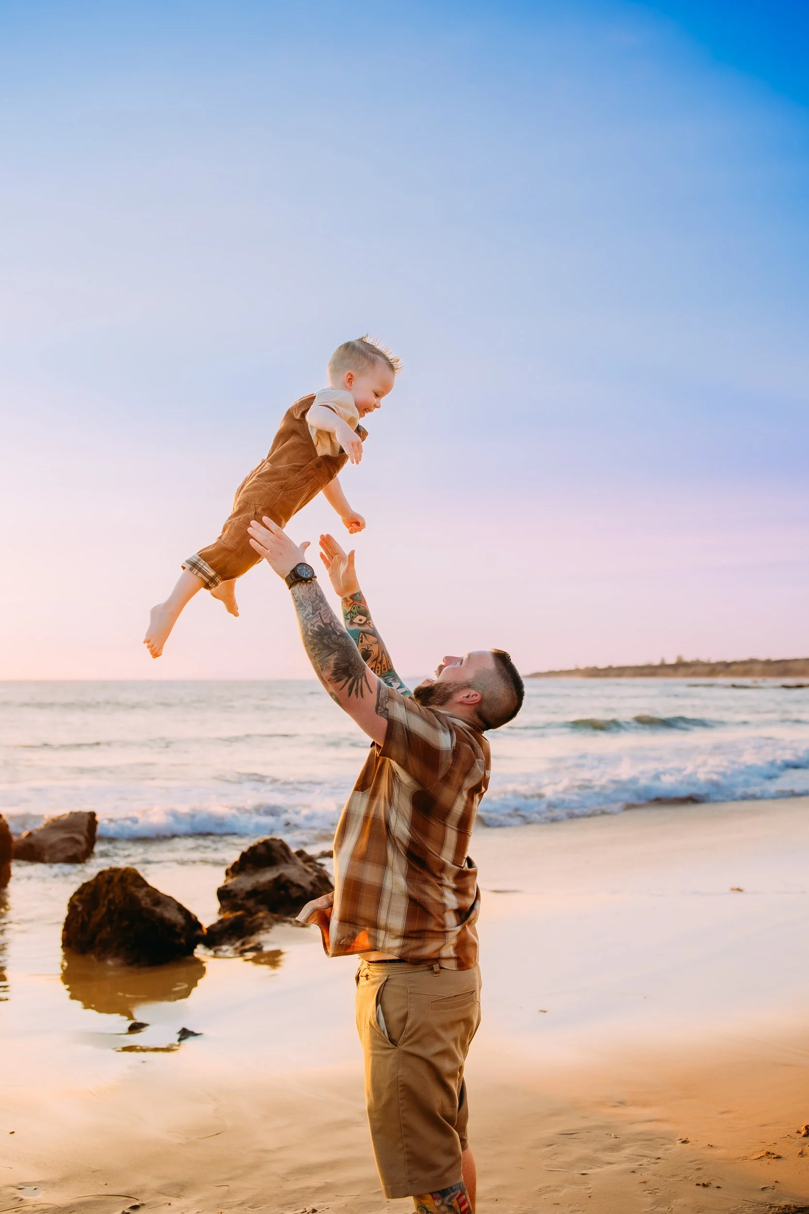 dad throwing his son into the air during their photo session together in Newport Beach, CA at sunset