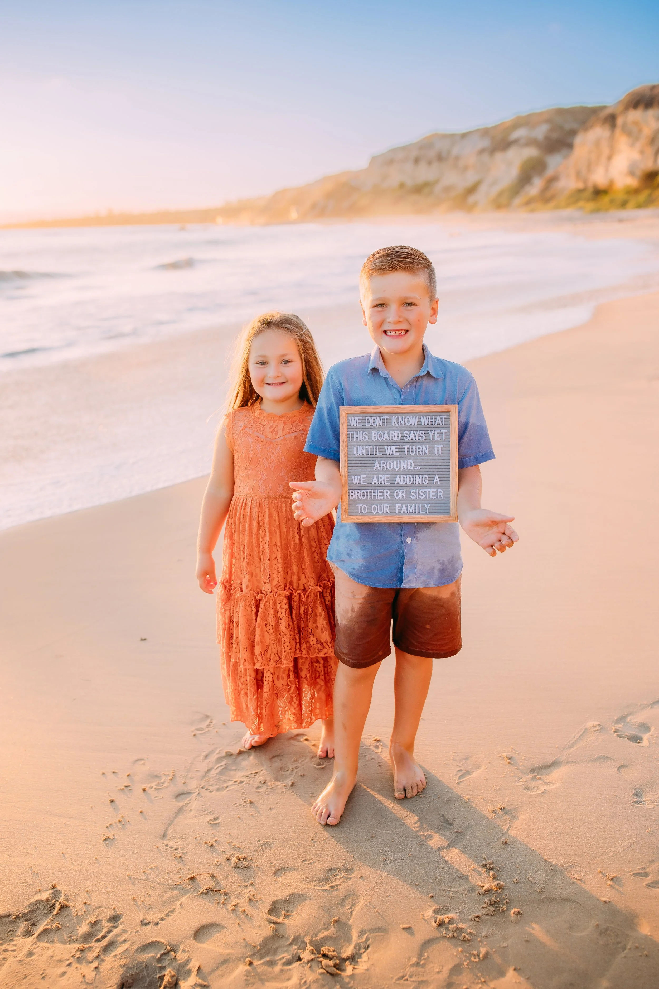 siblings holding a sign with a baby announcement of their new brother or sister during a baby announcement photo session in Newport Beach, CA