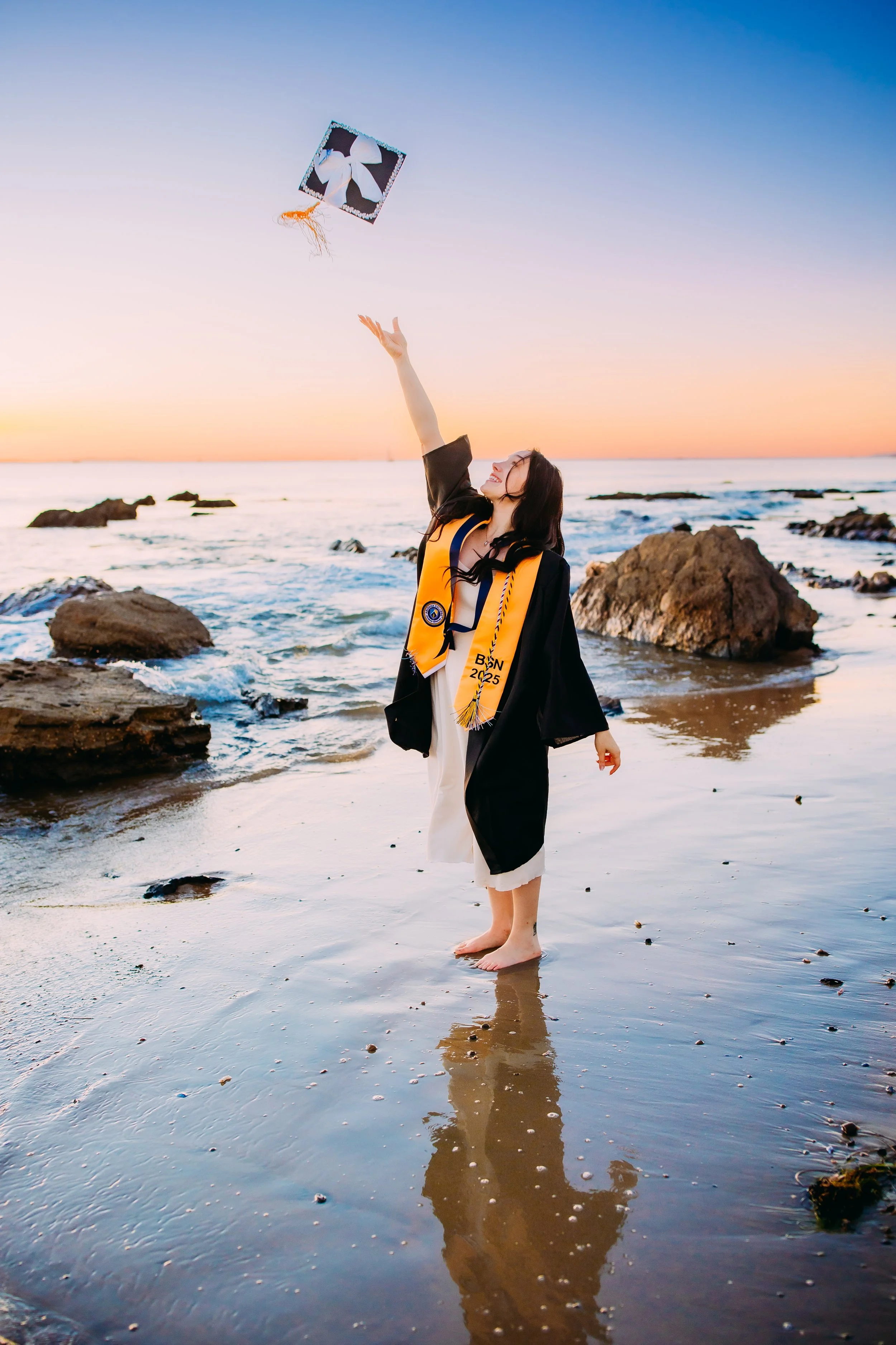 graduating senior girl throwing her cap into the air at Newport Beach's sunset ocean