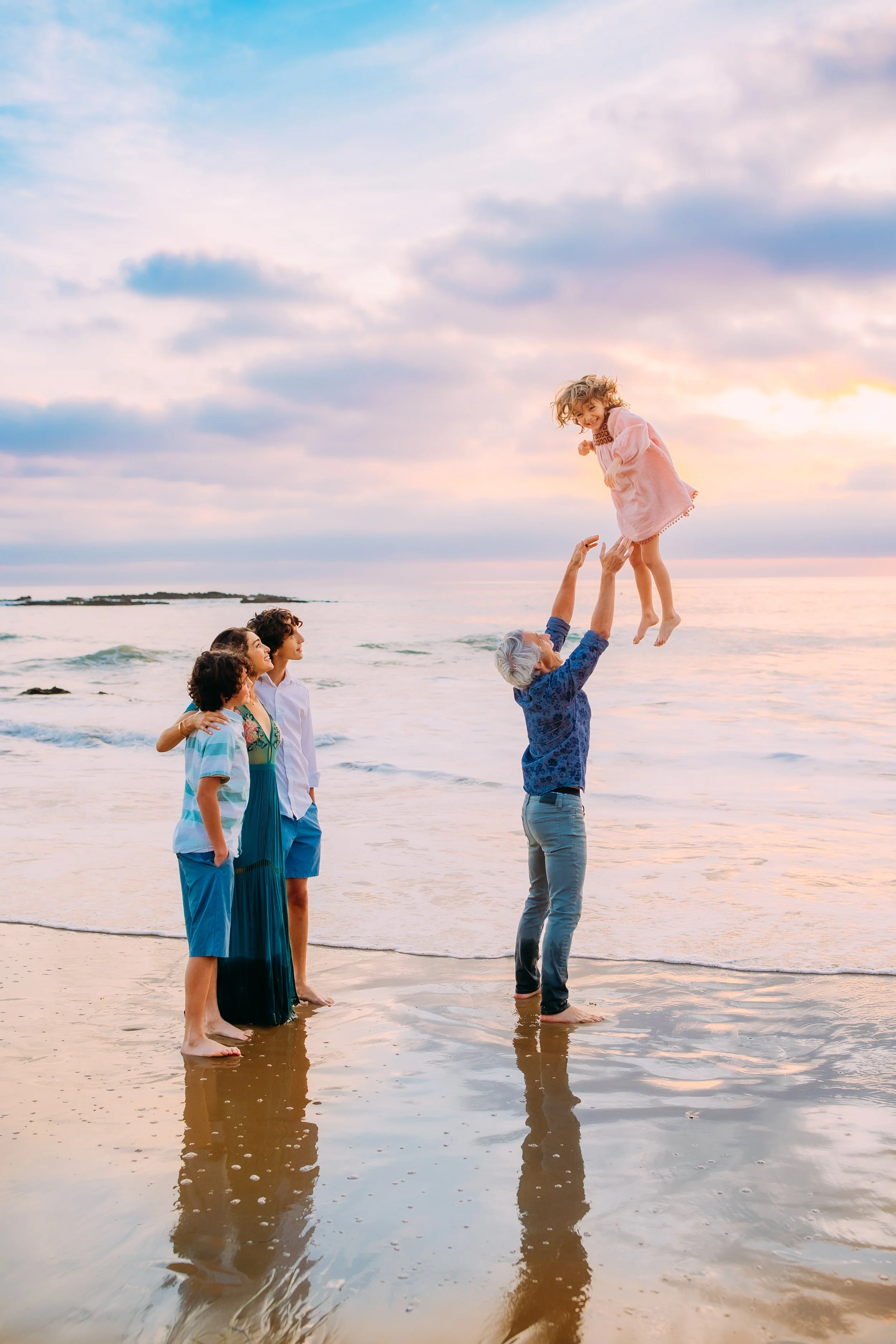 dad throwing his daughter playfully into the air while mom and brothers watch during their family photos in Newport Beach, California