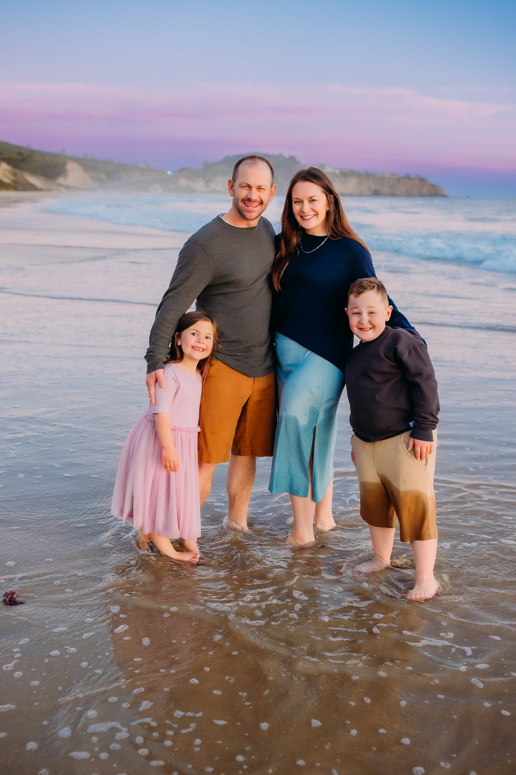 family posing for the camera with big smiles as the sun just set during their photo session in Newport Beach.