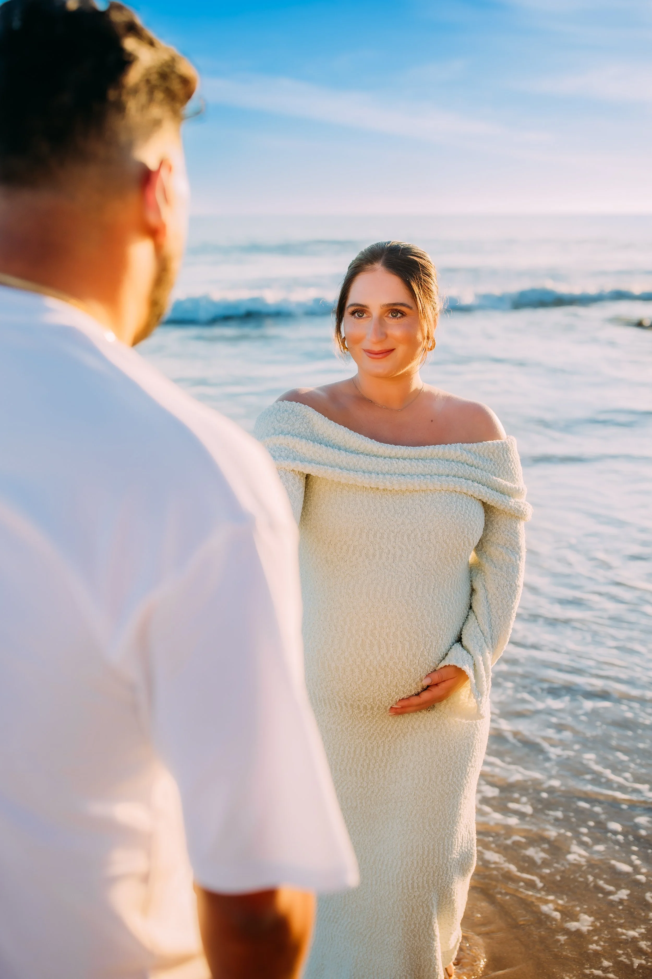 pregant mom being led for a walk along the ocean tide by her husband at their couple's maternity photoshoot in Newport Beach, California