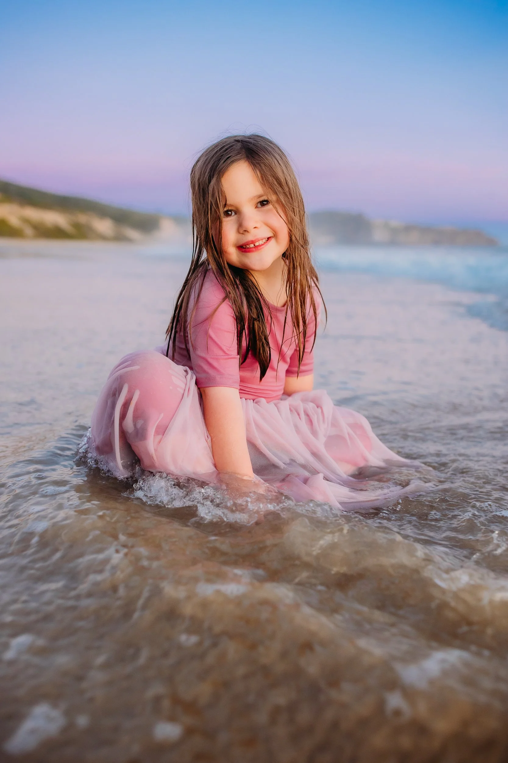little girl smiling smiling and soaked from the ocean wave during her sunset family photo session in Newport Beach.