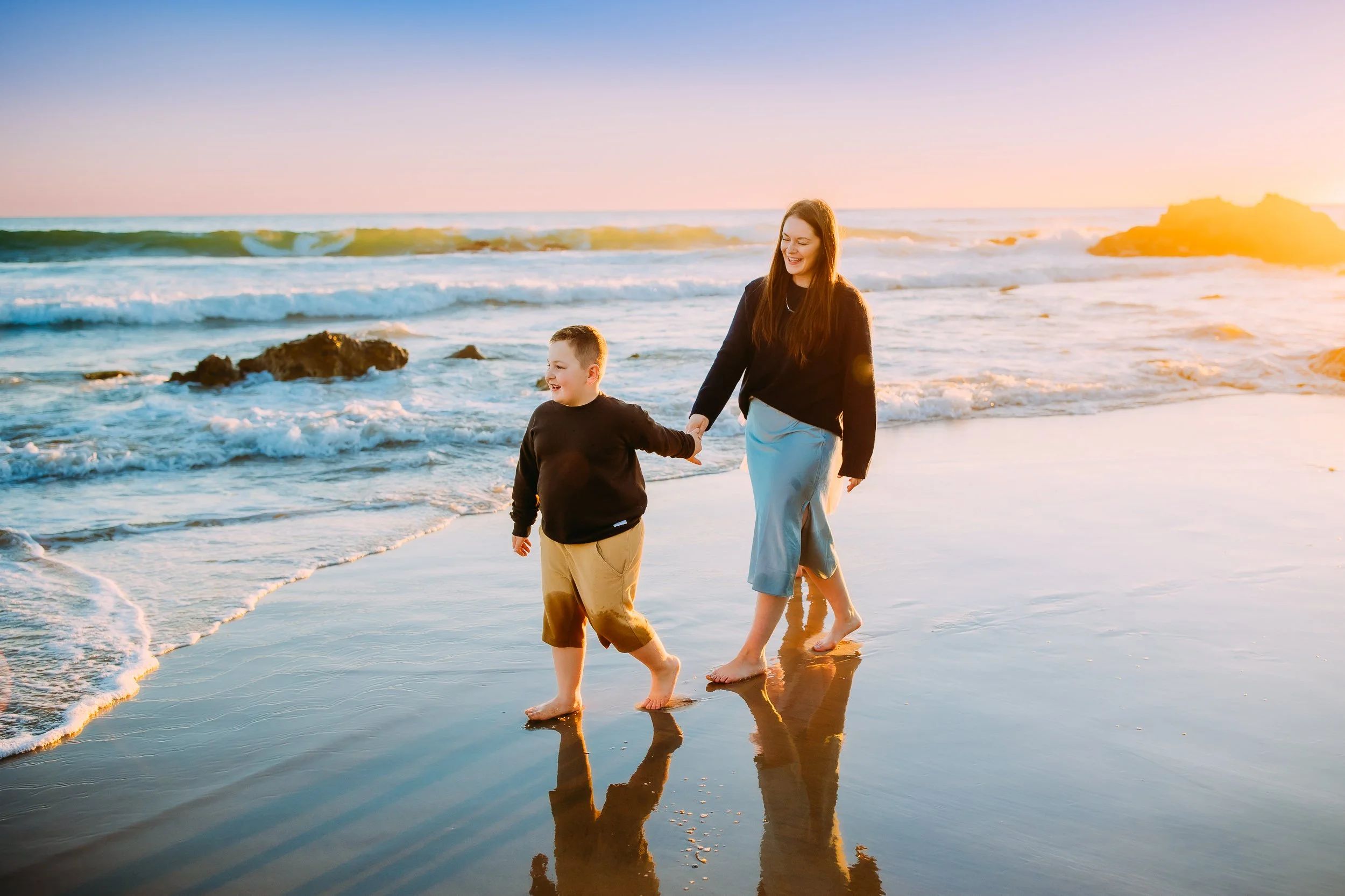 mom and son going for a walk along the ocean tide during their sunset photo session in Newport Beach.