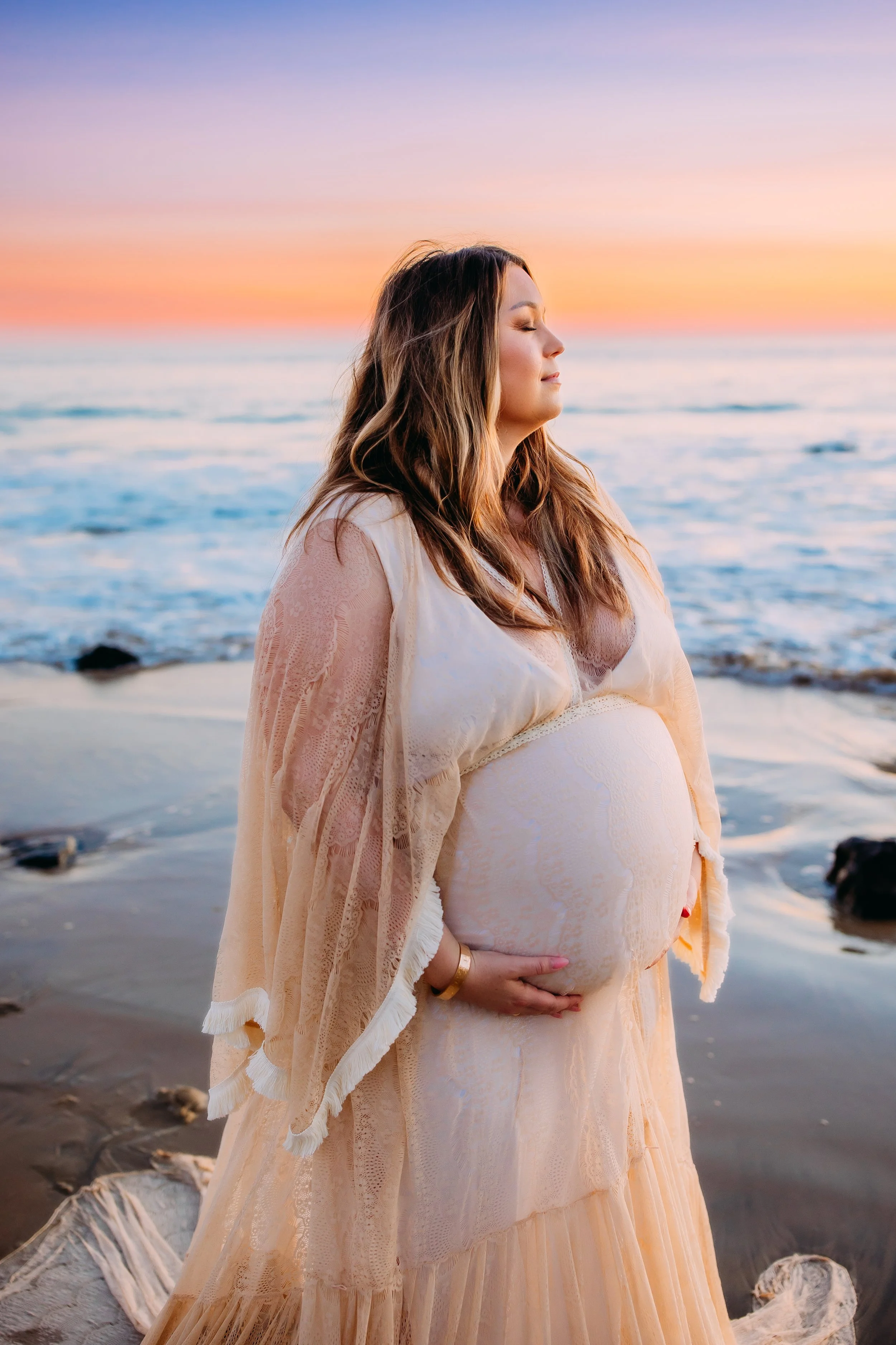 pregnant lady softly closing her eyes with her face towards the sunset during her beach photoshoot in Newport Beach, Orange County, California