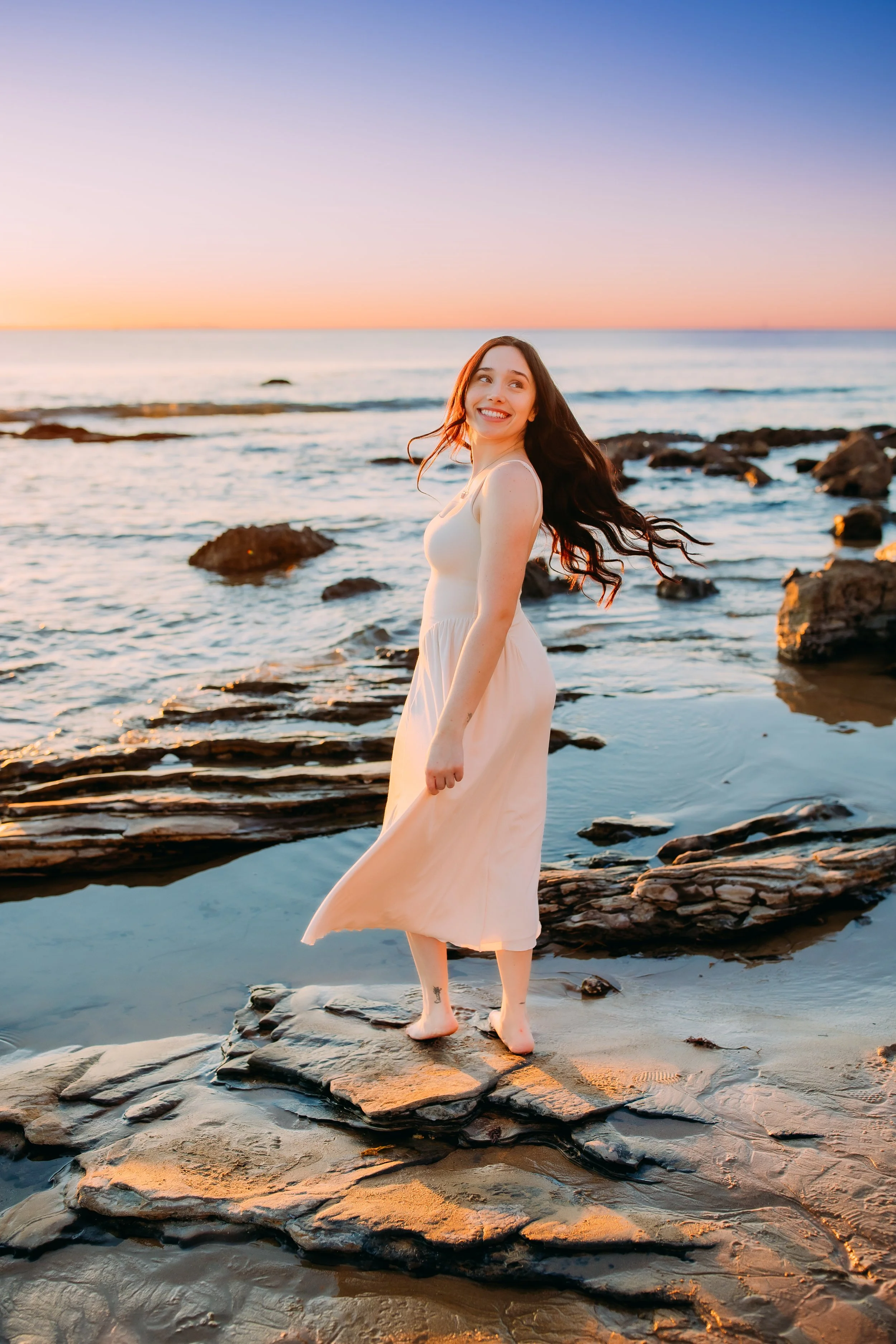 girl tossing her hair at sunset standing on rocks overlooking Newport Beach, California's Pacific Ocean
