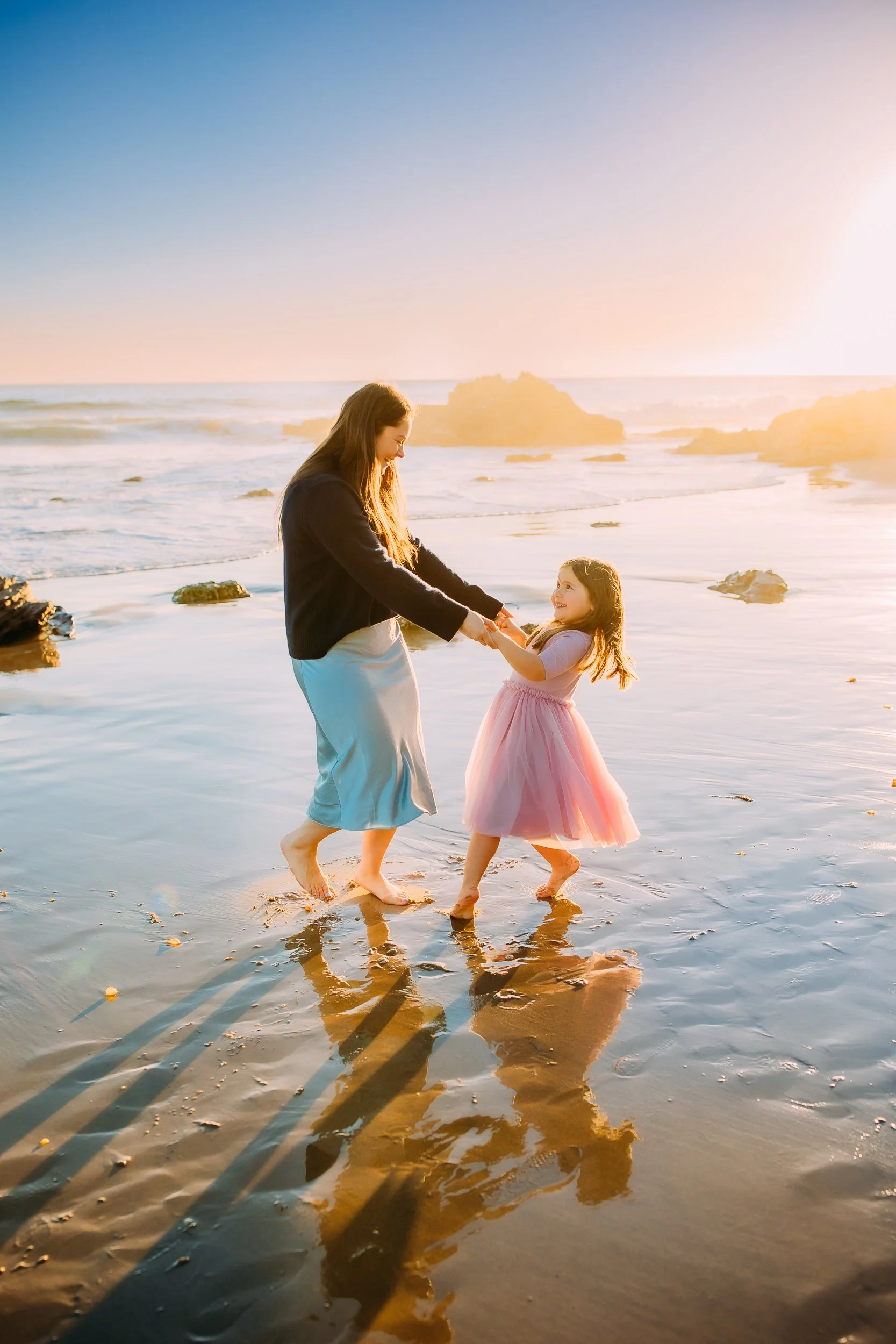 Mom and daughter laughing and spinning at the sunset during their photoshoot on the beach in Newport Beach.