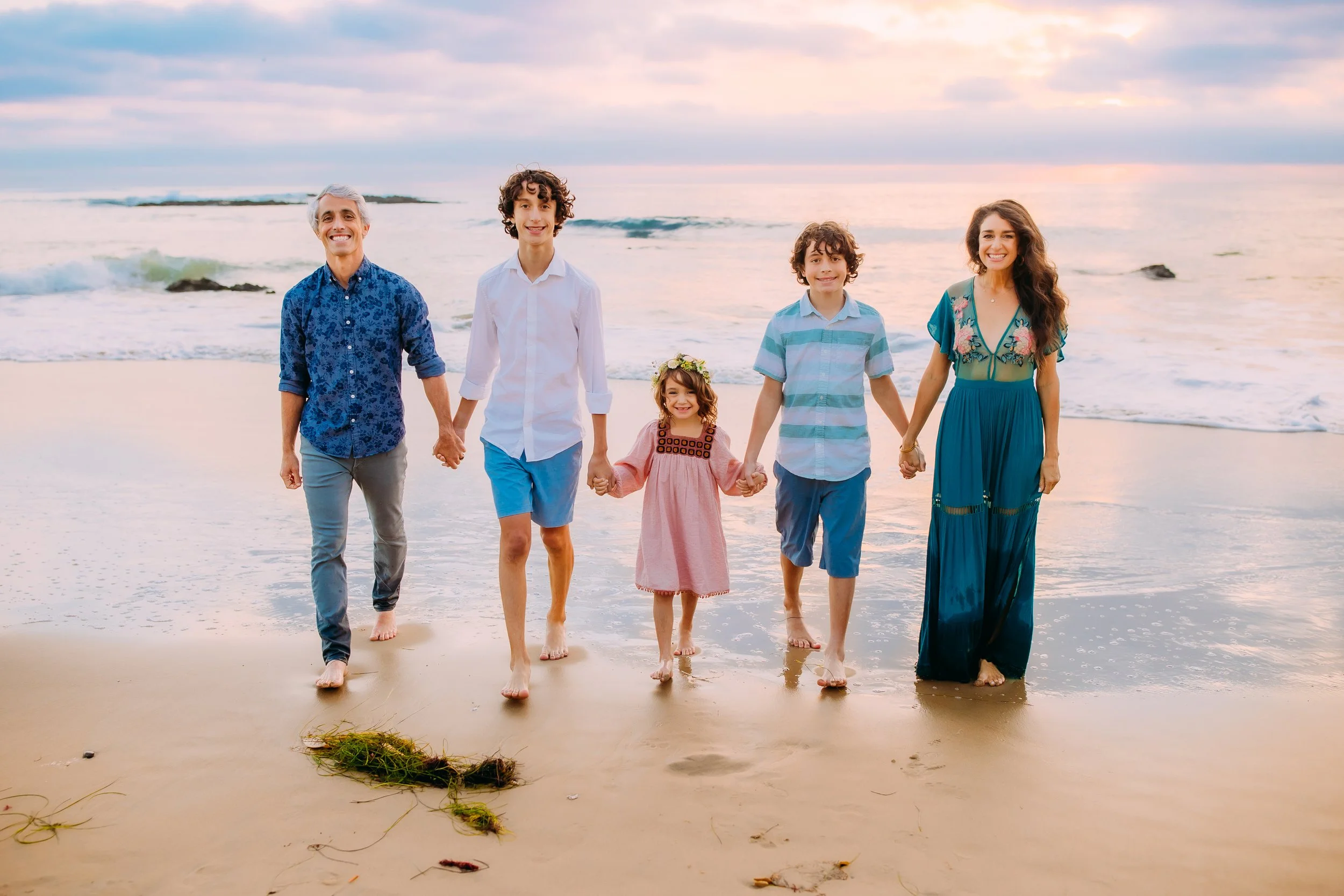 family holding hands and walking together at the ocean taking photos in Orange County, California
