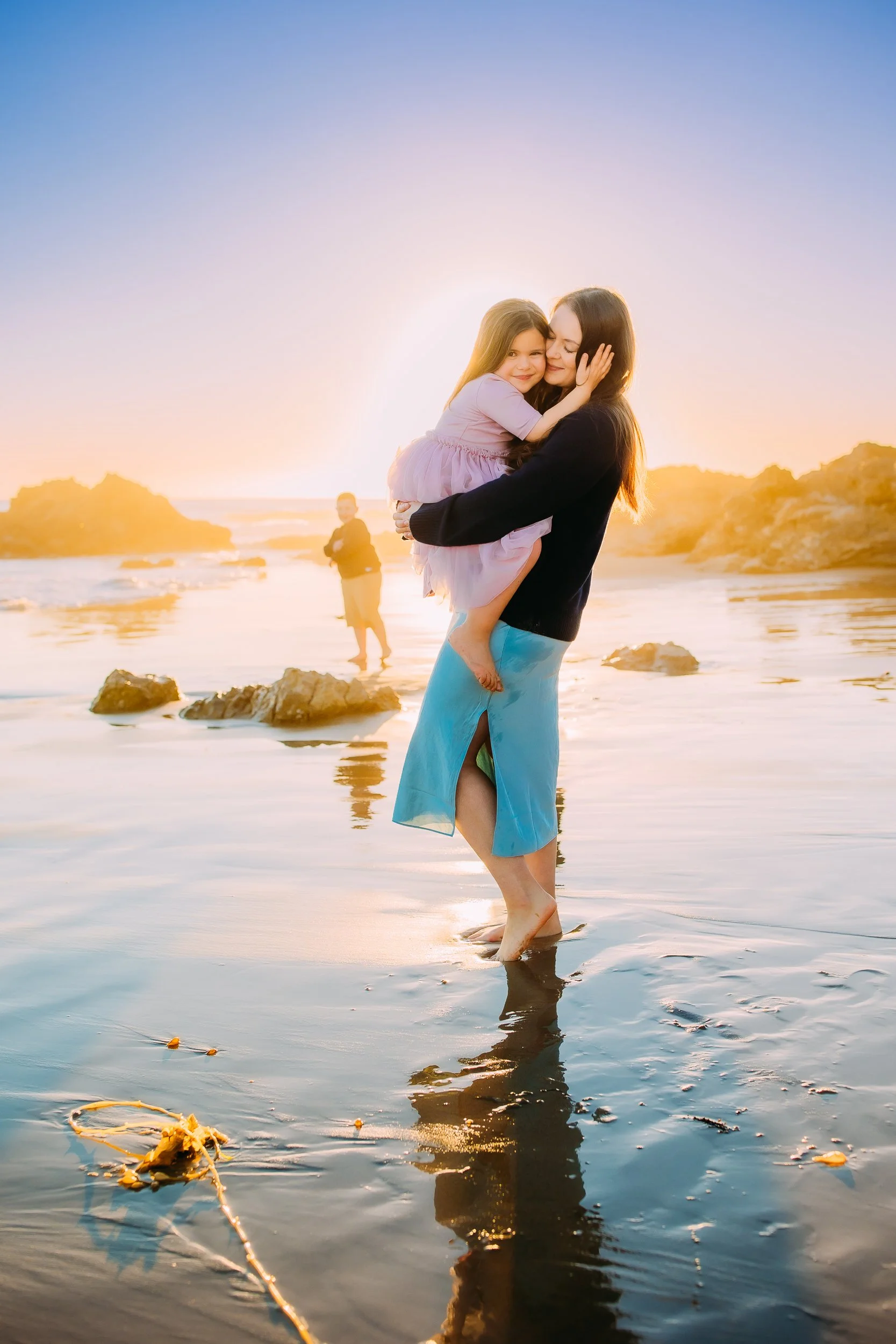 mom and daughter embracing one another with the sun setting behind them during their golden hour family photo session in Newport Beach.
