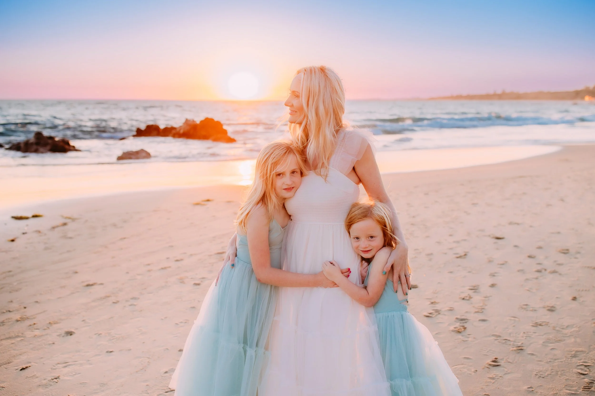 mom gazing out at the ocean while her daughters smile at the camera during their family photos in Newport Beach, California