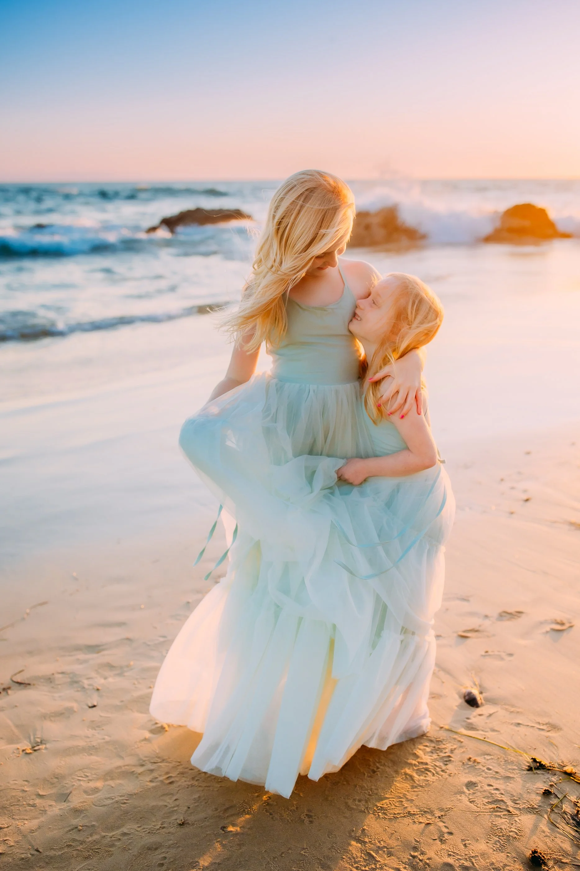 sisters happily embracing during their sunset photo session along the shores of Newport Beach in Orange County, California