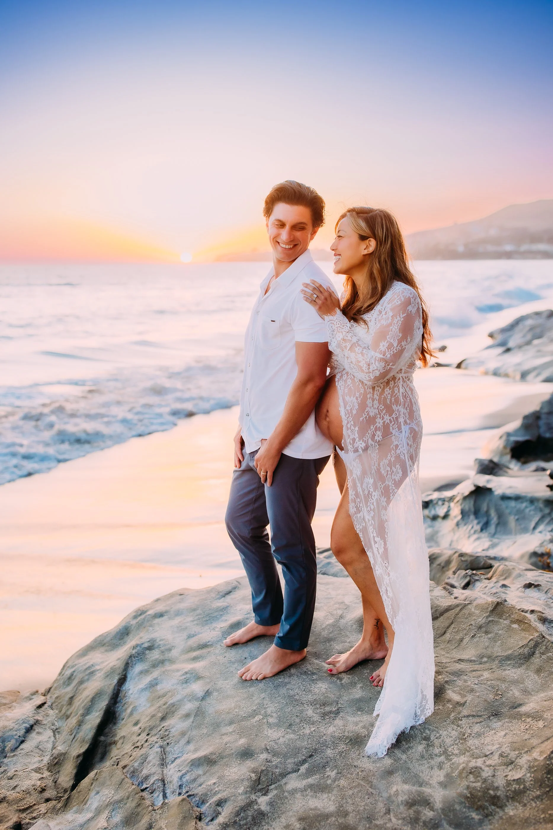 mom and dad to be laughing together while standing on the rocks during their maternity photo session in Laguna Beach, California