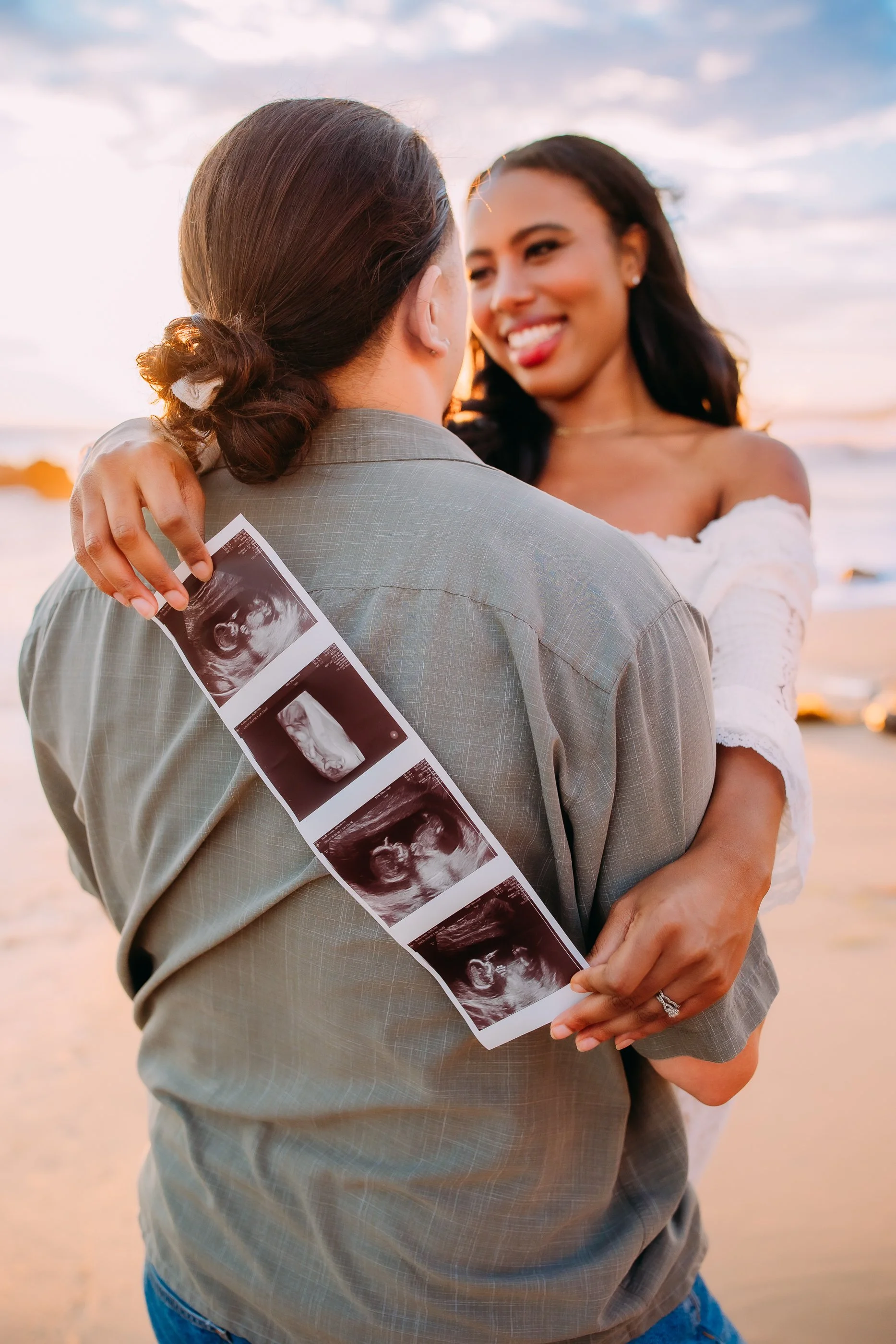 mom and dad to be holding an ultrasound picture during their sunset photoshoot in Newport Beach, California
