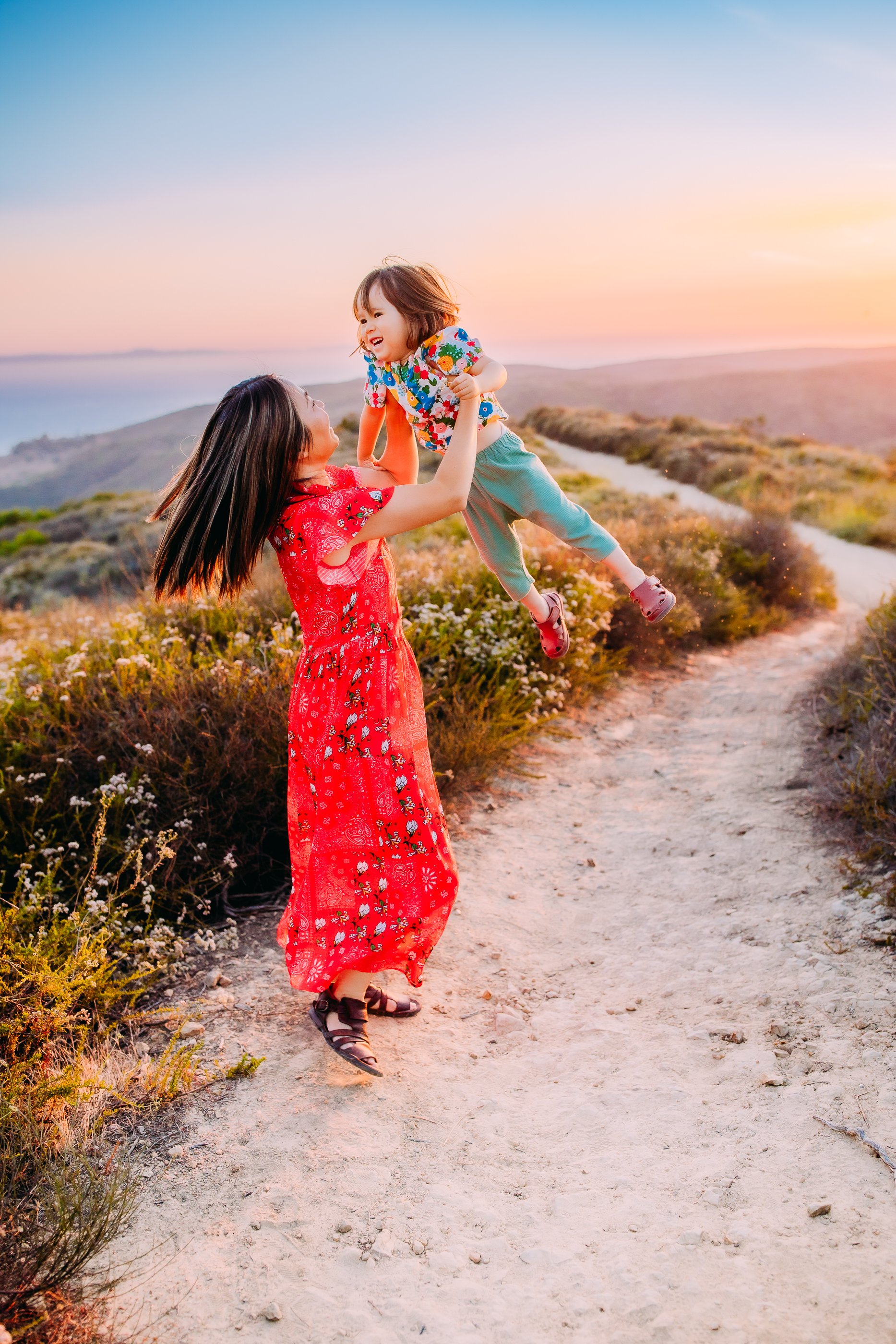 mother spinning her son into the air during their photo session at sunset in the foothills of Laguna Beach, California