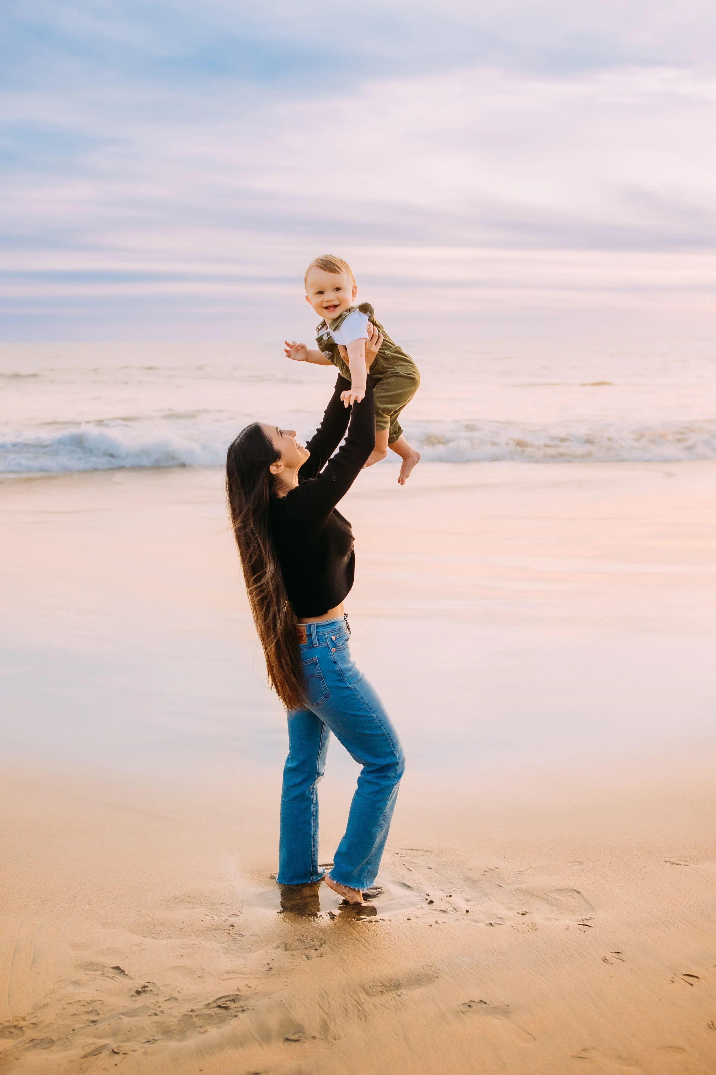 Mom cuddMother flying up her one-year-old during a mommy and me beach session in Newport Beach.