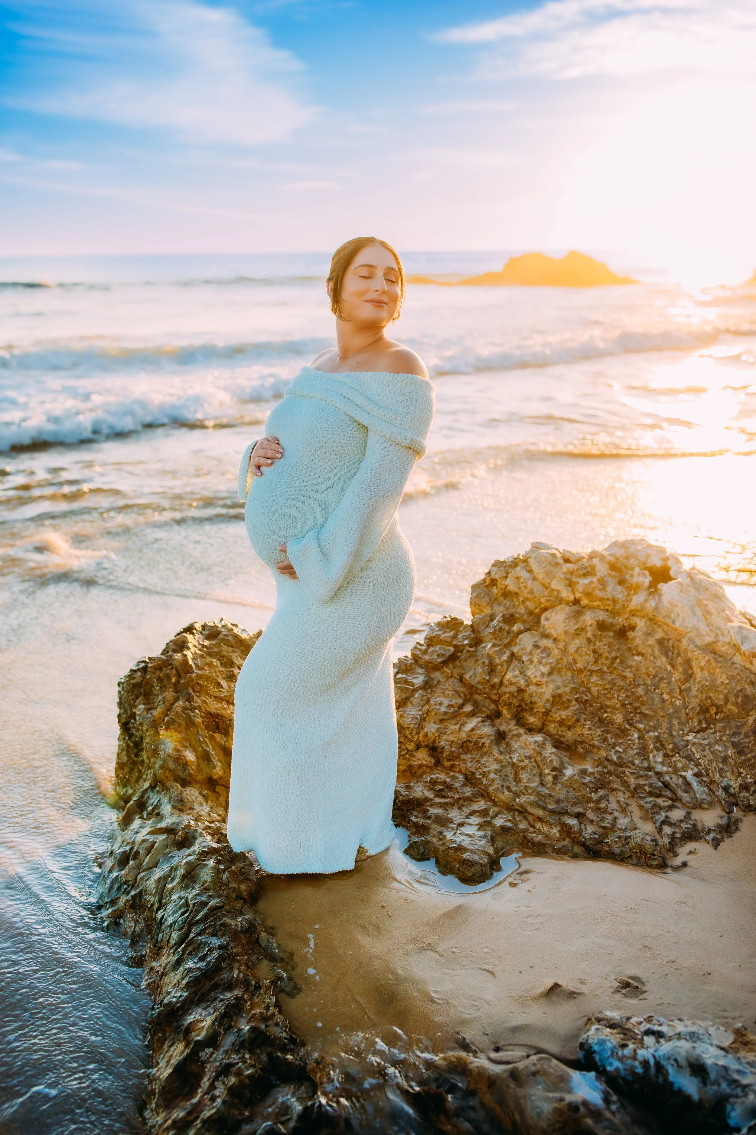 pregnant mom holding her belly and taking in the sunset during her photo session at the ocean in Orange County, California