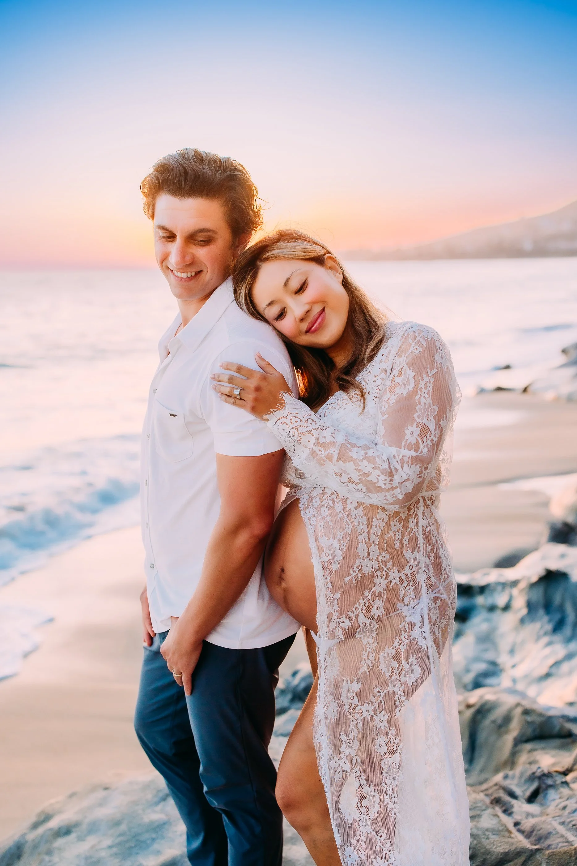 pregnant woman resting on her husband during their sunset photo session in Laguna Beach, California