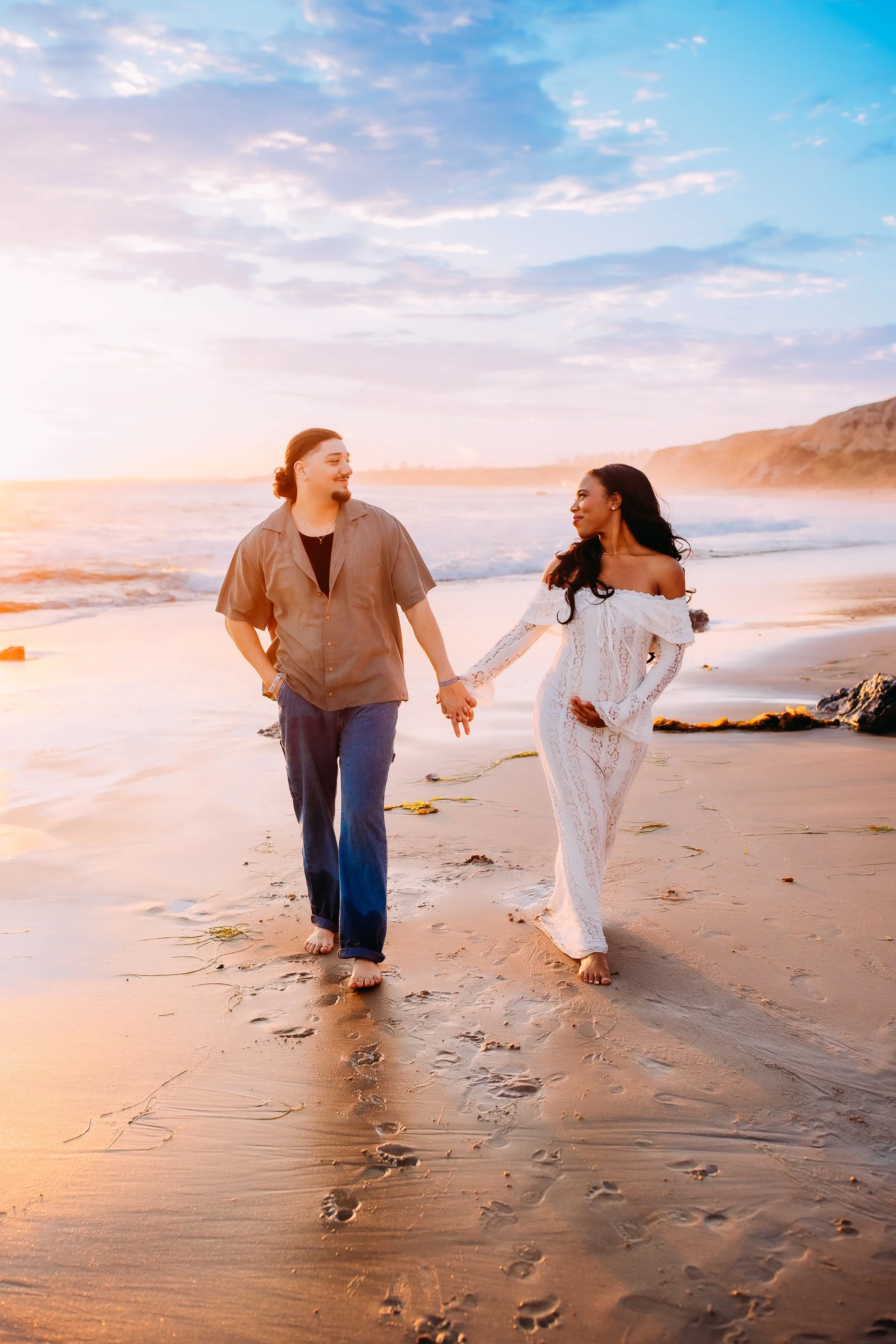 mom and dad to be walking along the shoreline at sunset during their pregnancy announcement photoshoot in Newport Beach, California