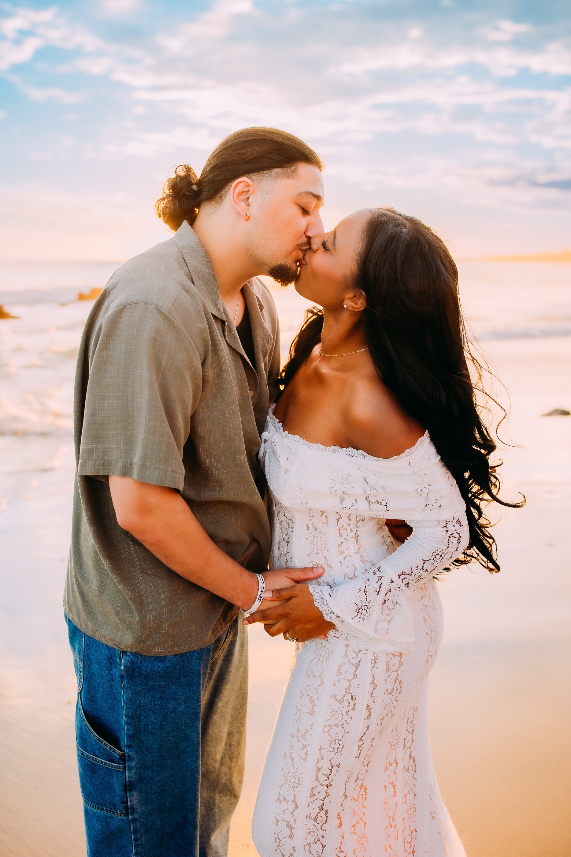 couple kissing with the sun setting behind them during their pregnancy reveal photoshoot in Newport Beach, California