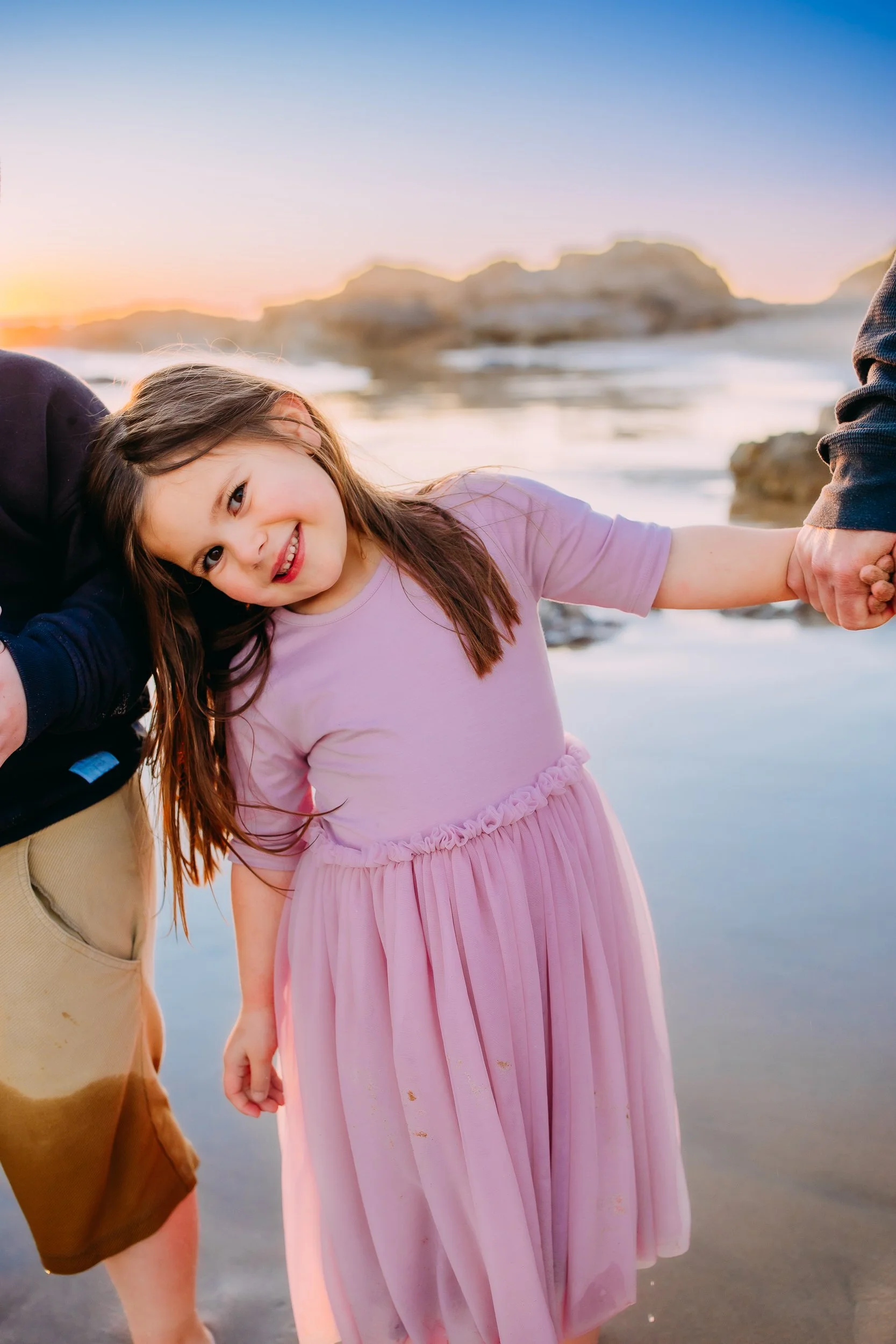 close up photo of girl while she holds her dad's hand and smiles at the camera during their family photoshoot in Newport Beach.