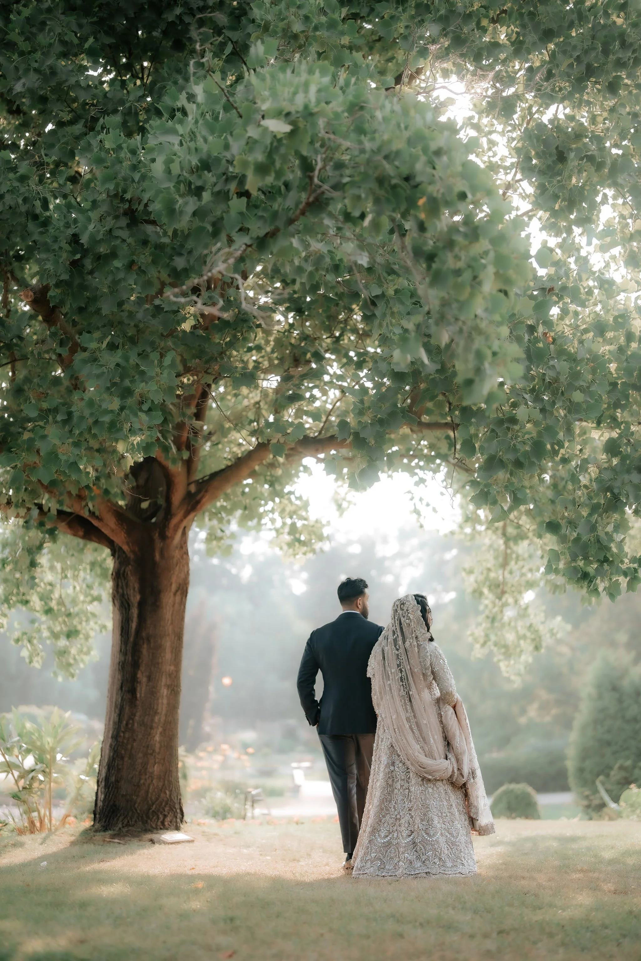 Muslim wedding photography Toronto – bride and groom walking hand in hand under trees at sunset.