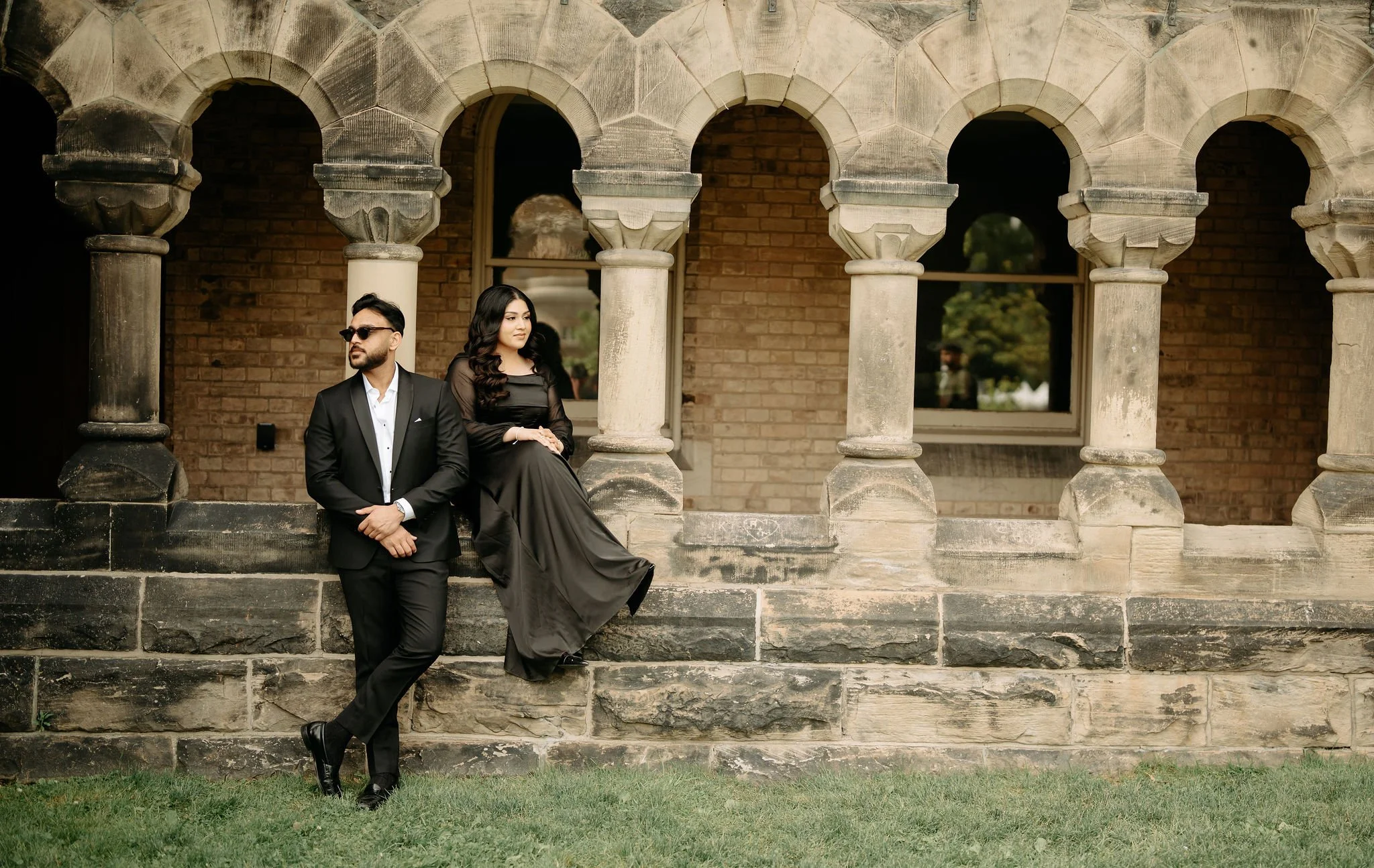Muslim wedding photographer Toronto – bride and groom in black formal attire at historic stone arches.
