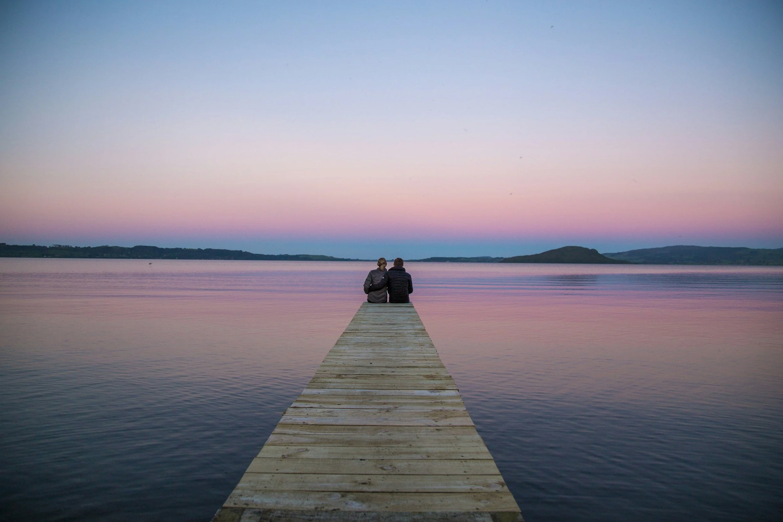 Photo of a pier over water with with individuals sitting next to each other.