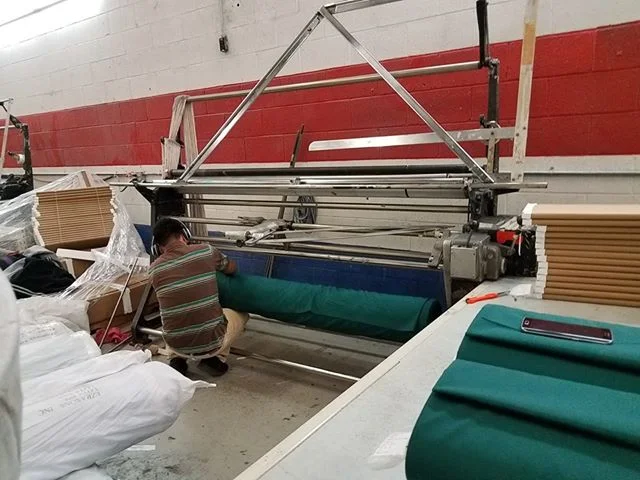 This is the machine that the big rolls are put on so that they can then unrolled from and put on to the small cardboard bolts. Here the guy is putting the roll on the bottom and starting to feed it through the rollers.