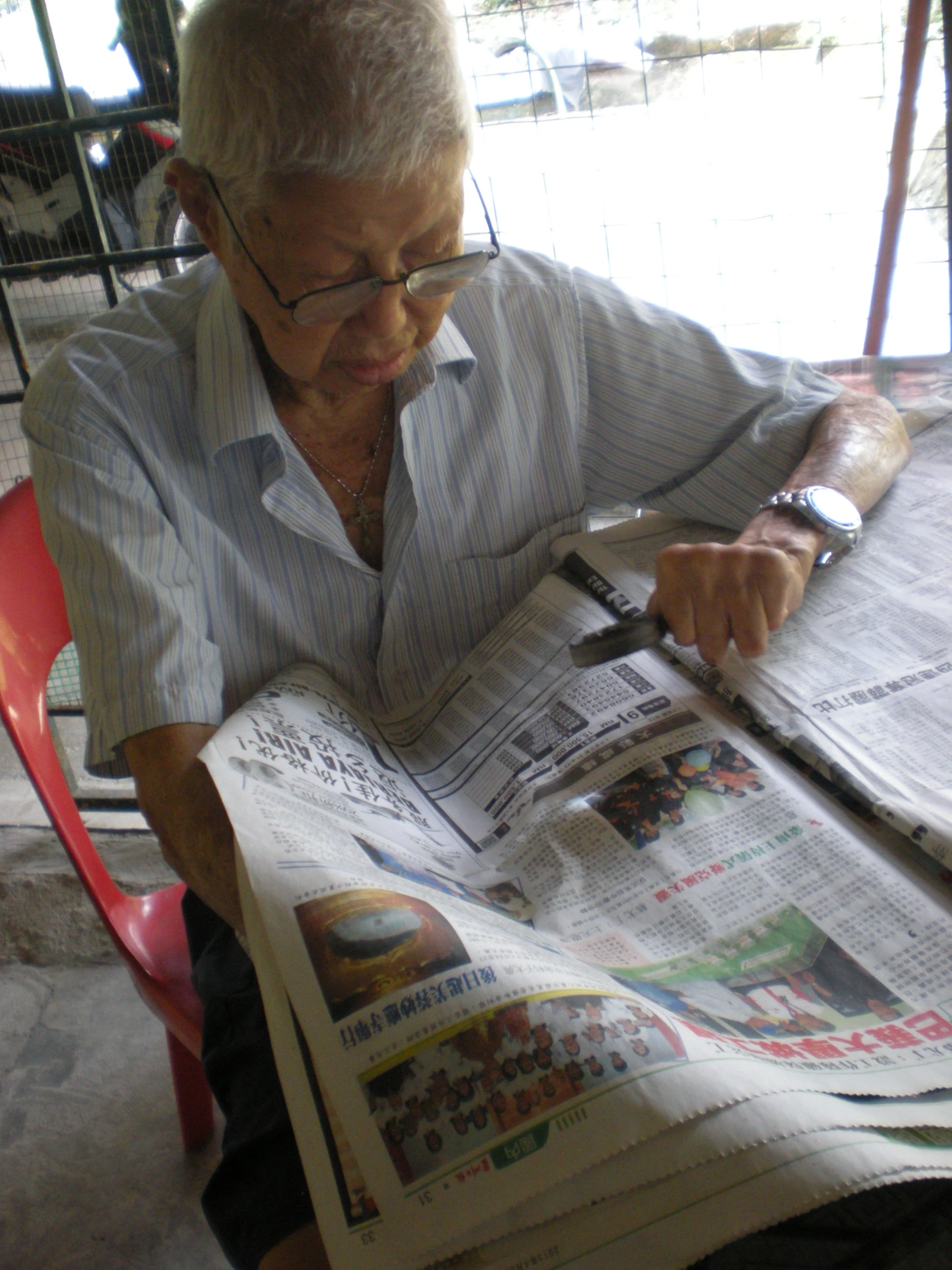 Lam reading the papers with a magnifying glass. (photo by Tan Ean Nee)