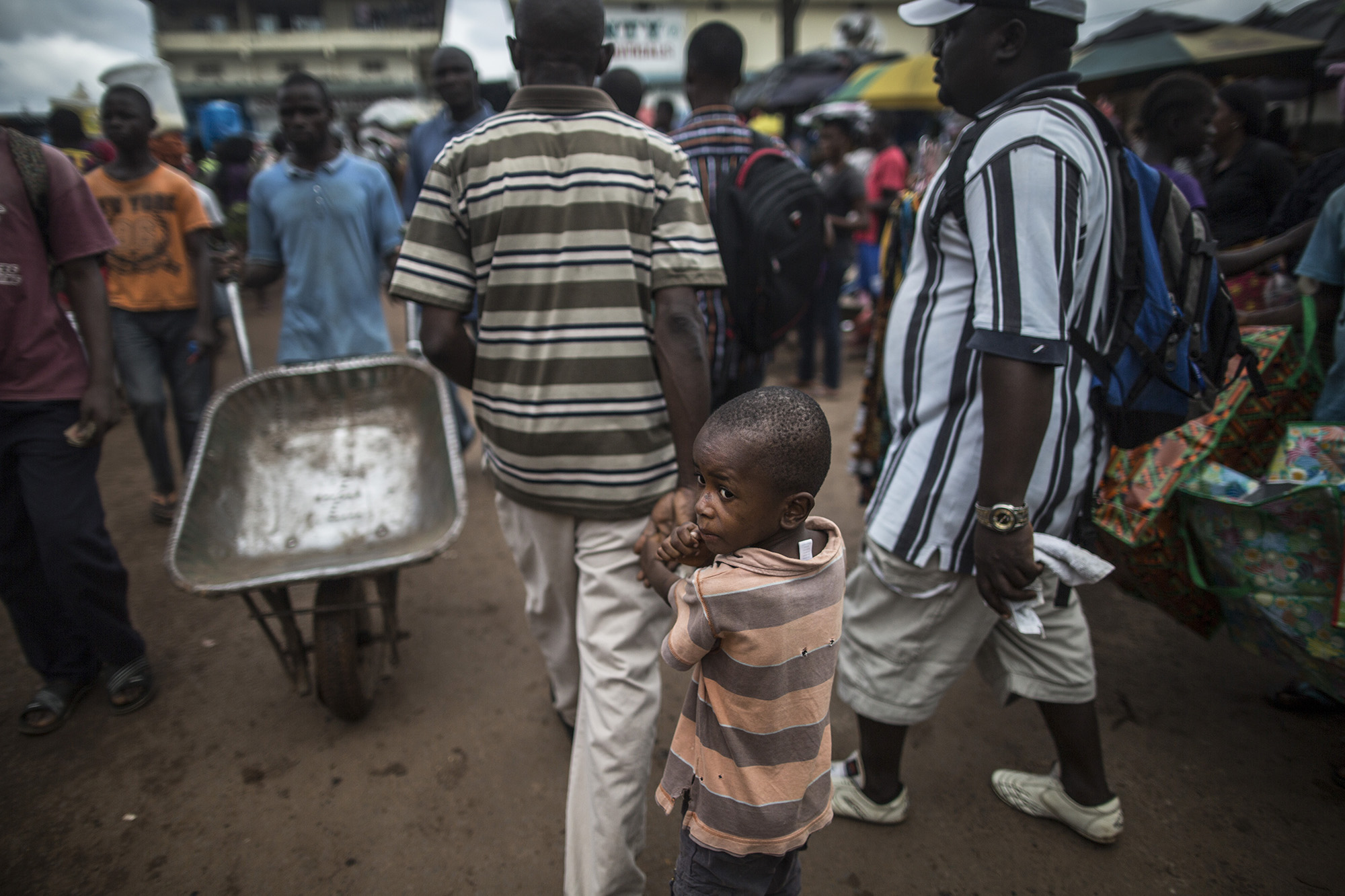  Patrick Poopei, 7, walks with his father, William, through the Red Light District in Liberia. When William's uncle became ill in 2014 and traveled to Monrovia for care, his wife took care of him. She also became ill.&nbsp;William took his wife to se