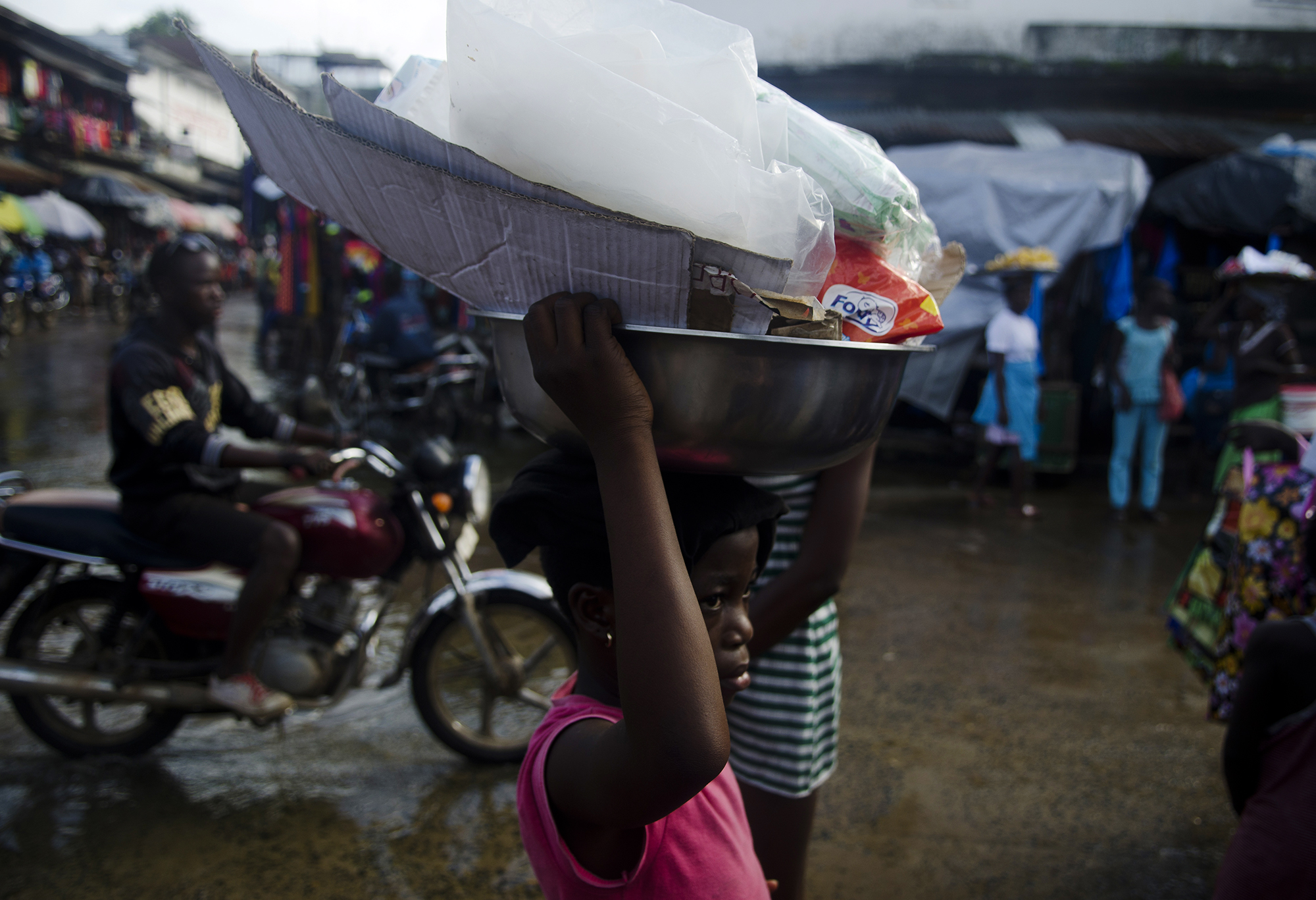  A girl walks through the waterside market in Liberia to sell goods.&nbsp;According to the WHO, approximately 64 percent of Liberians live below the poverty line ($1.25/day).&nbsp;This poverty often leads parents to force their children to sell on th
