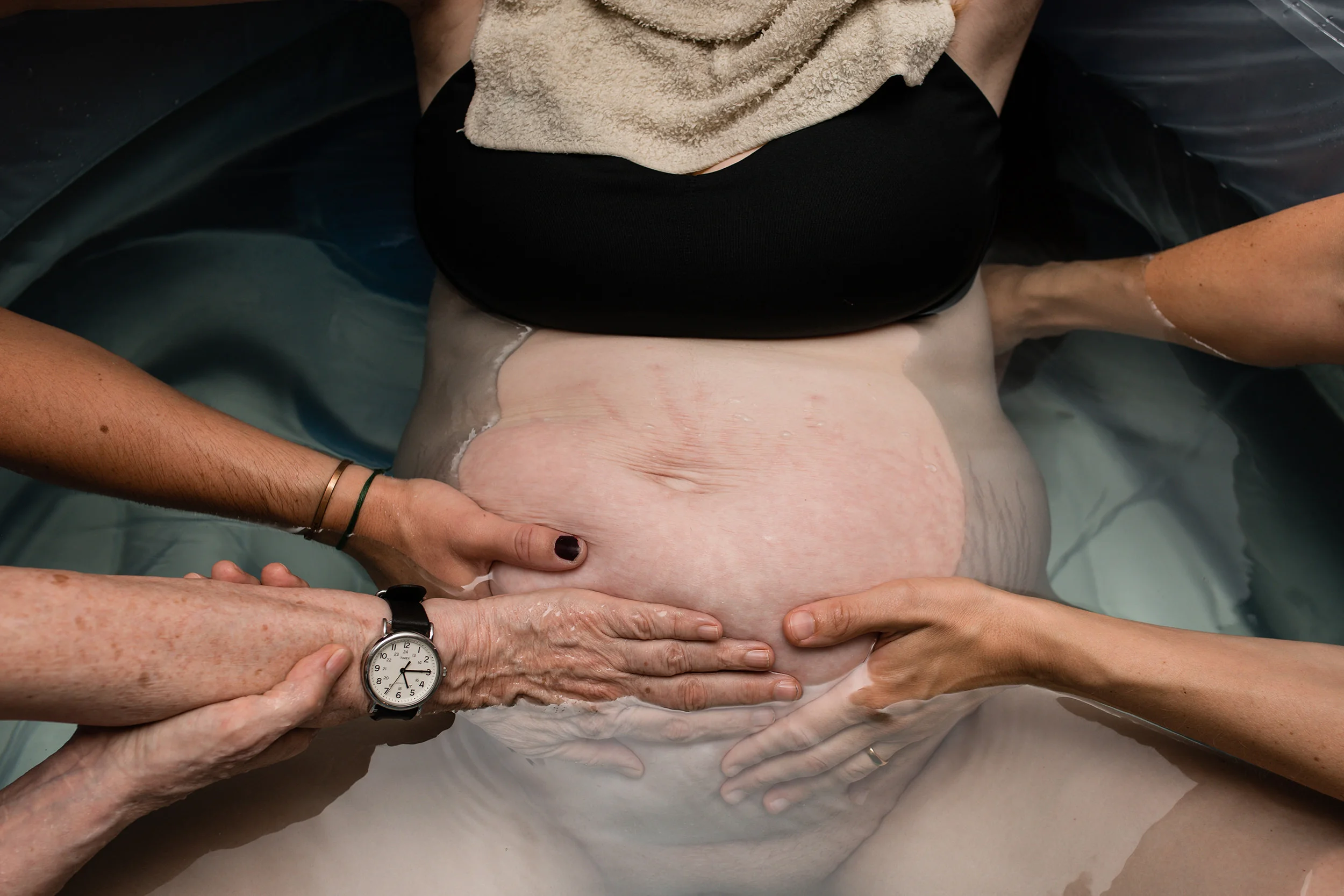 supportive hands on laboring mothers belly during home water birth