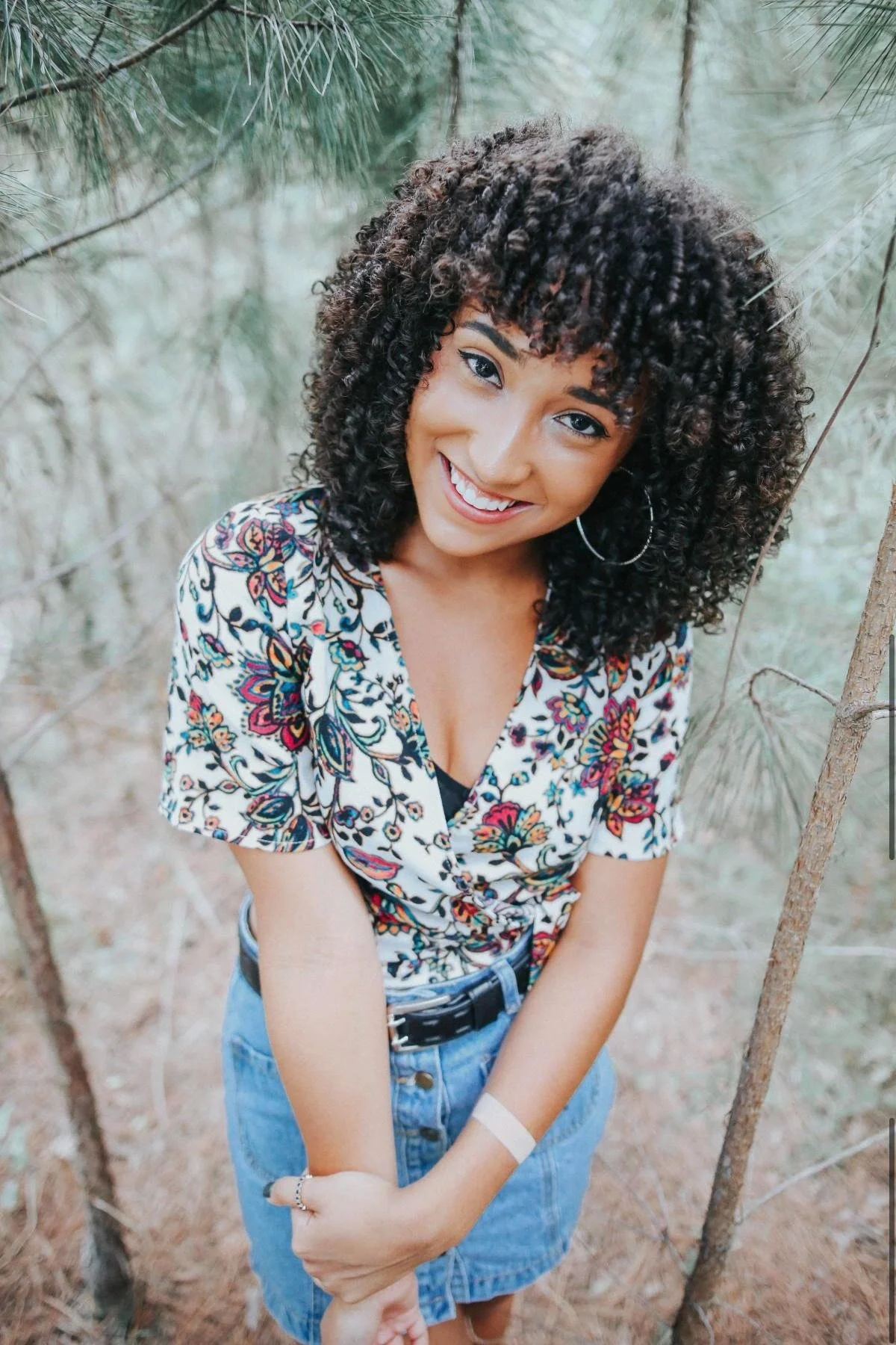 Portrait of a woman with curly hair smiling in a wooded setting, Orkams collab series