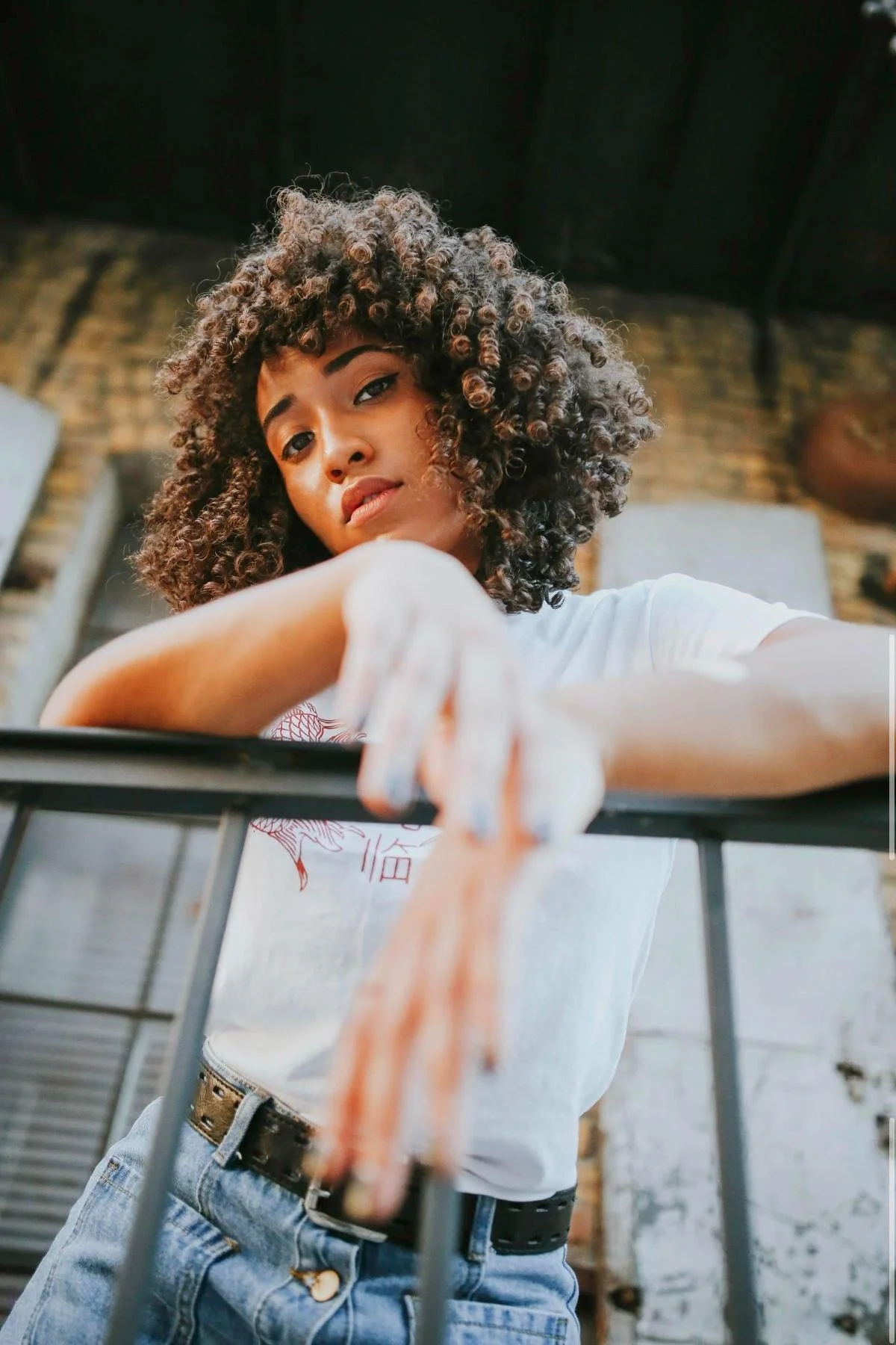 Portrait of a woman with curly hair leaning against an urban railing, Orkams collab series