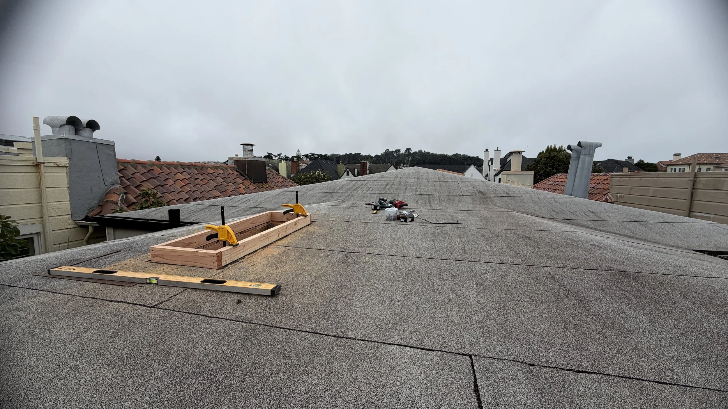 Where there is insufficient roof pitch, a wood "curb" will serve as a weather-resistant transition between the skylight and the roof.

The skylight will drop atop the curb and be fastened on the sides. 