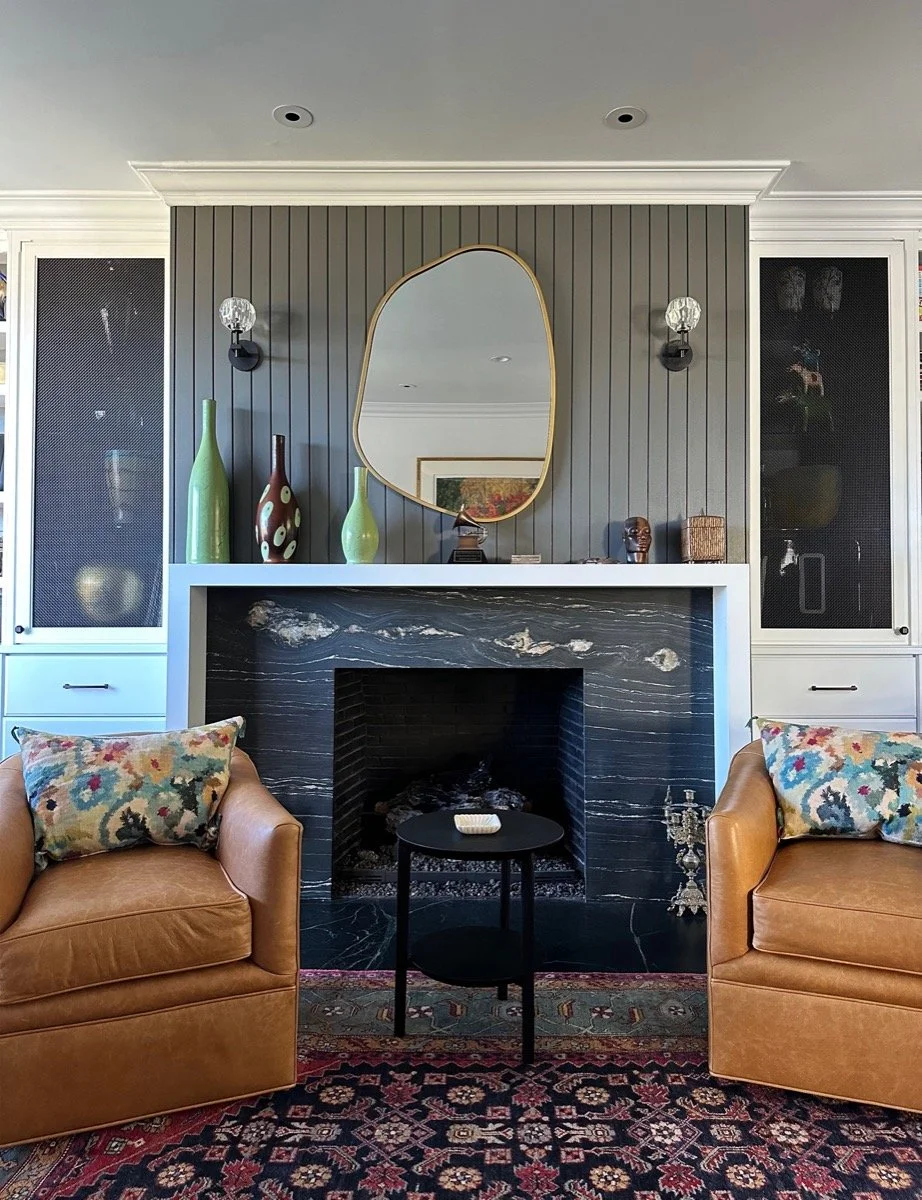  A gray fireplace with an organic shaped mirror. 