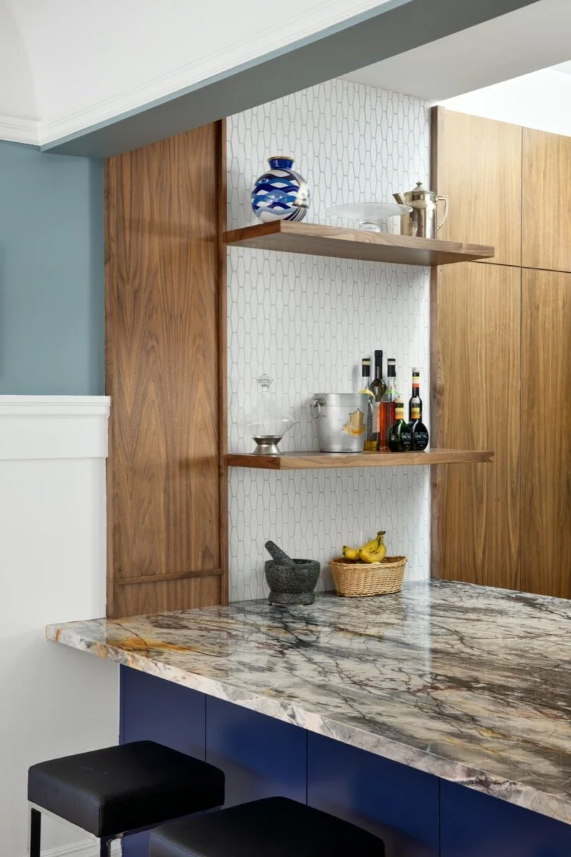  The kitchen is a mix of medium toned wood, heavily veined marble, navy and stainless steel. 