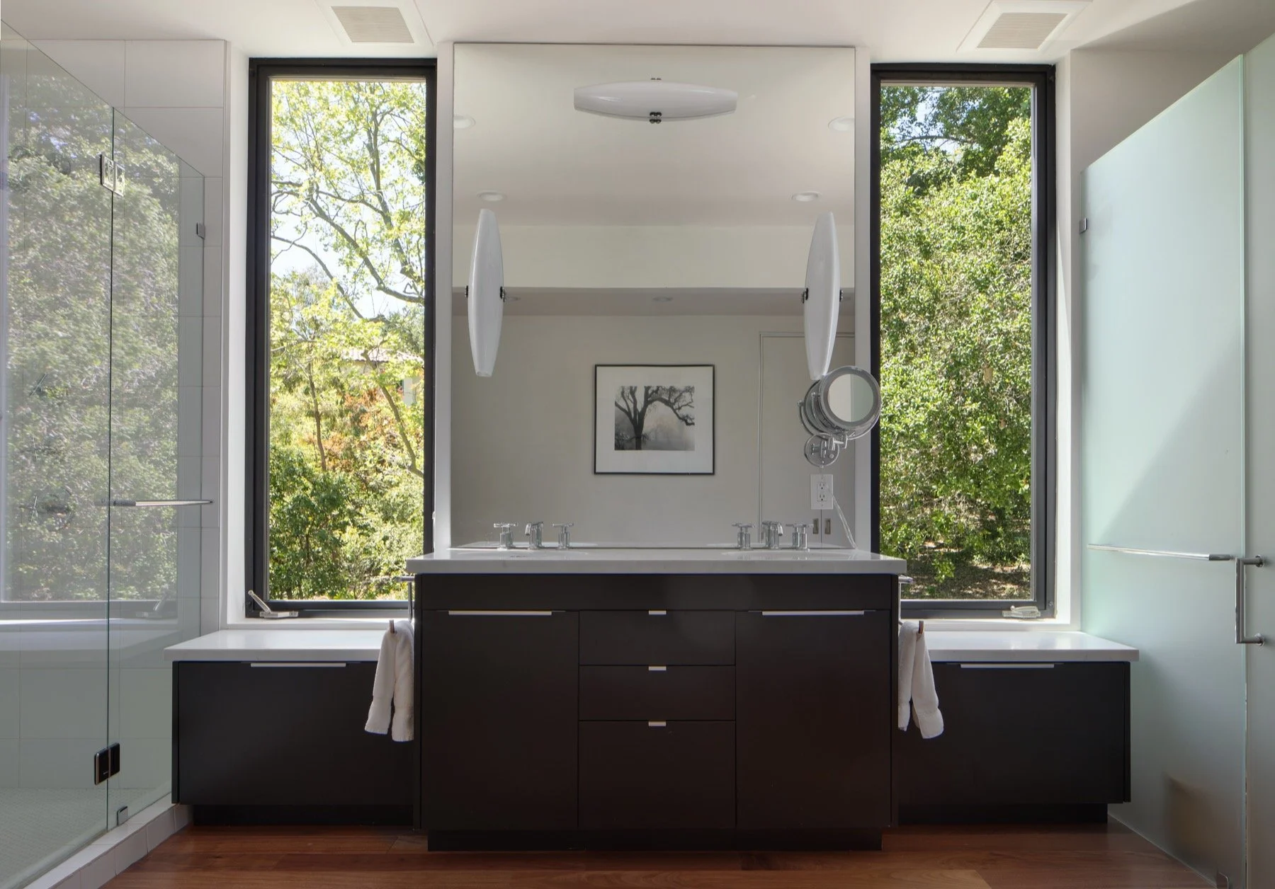  In the bathroom, the sink/vanity is framed by two tall windows with views of the trees. 