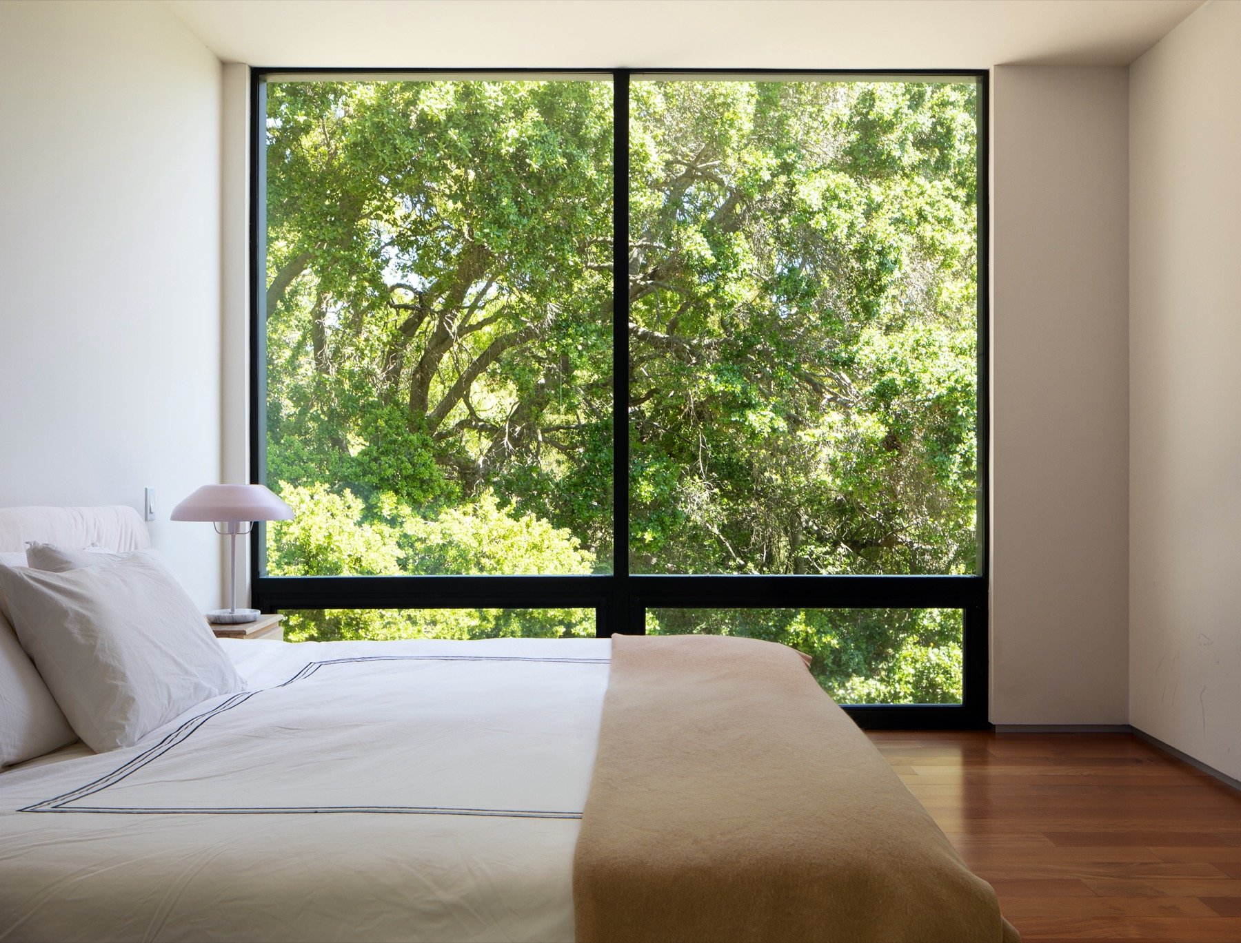  A bedroom as a full window wall, looking out into the treetops. 
