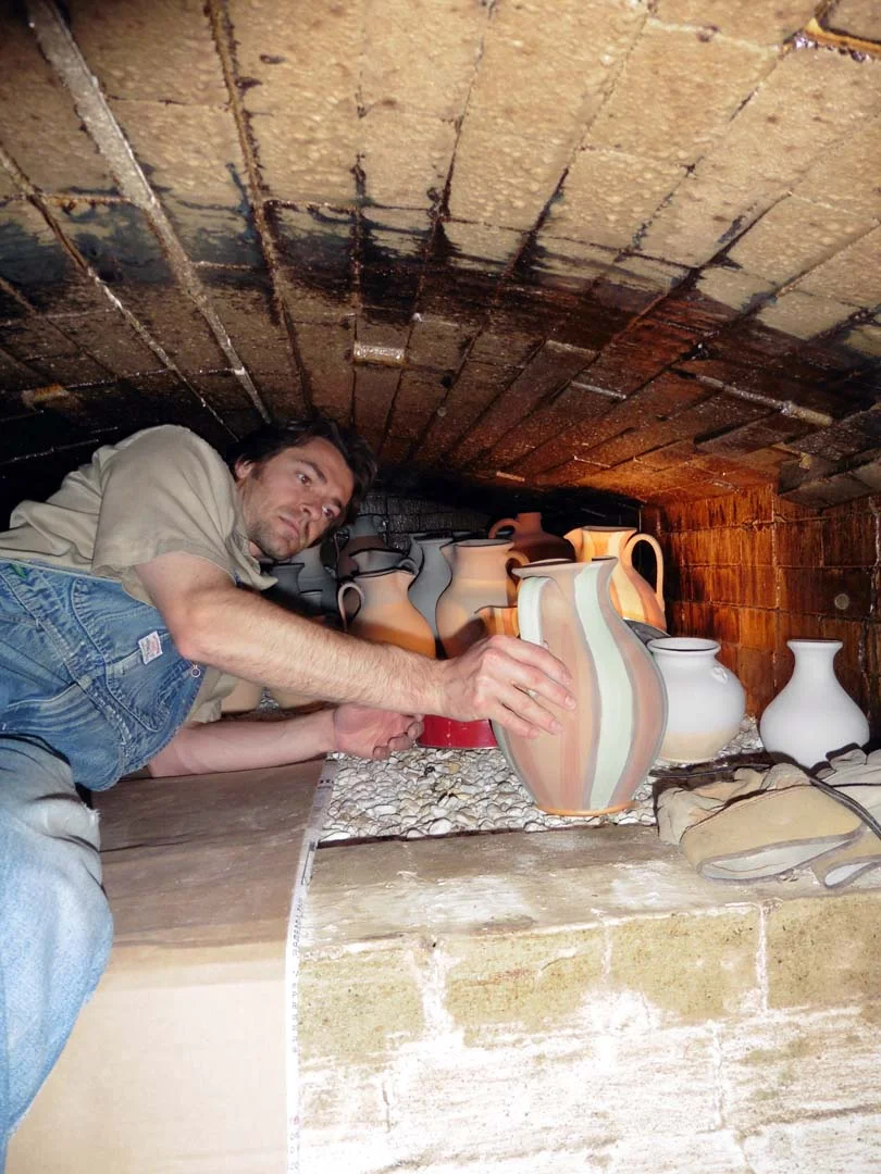 Travis in the wood kiln placing the pots on crushed flint rock for a salt glaze firing