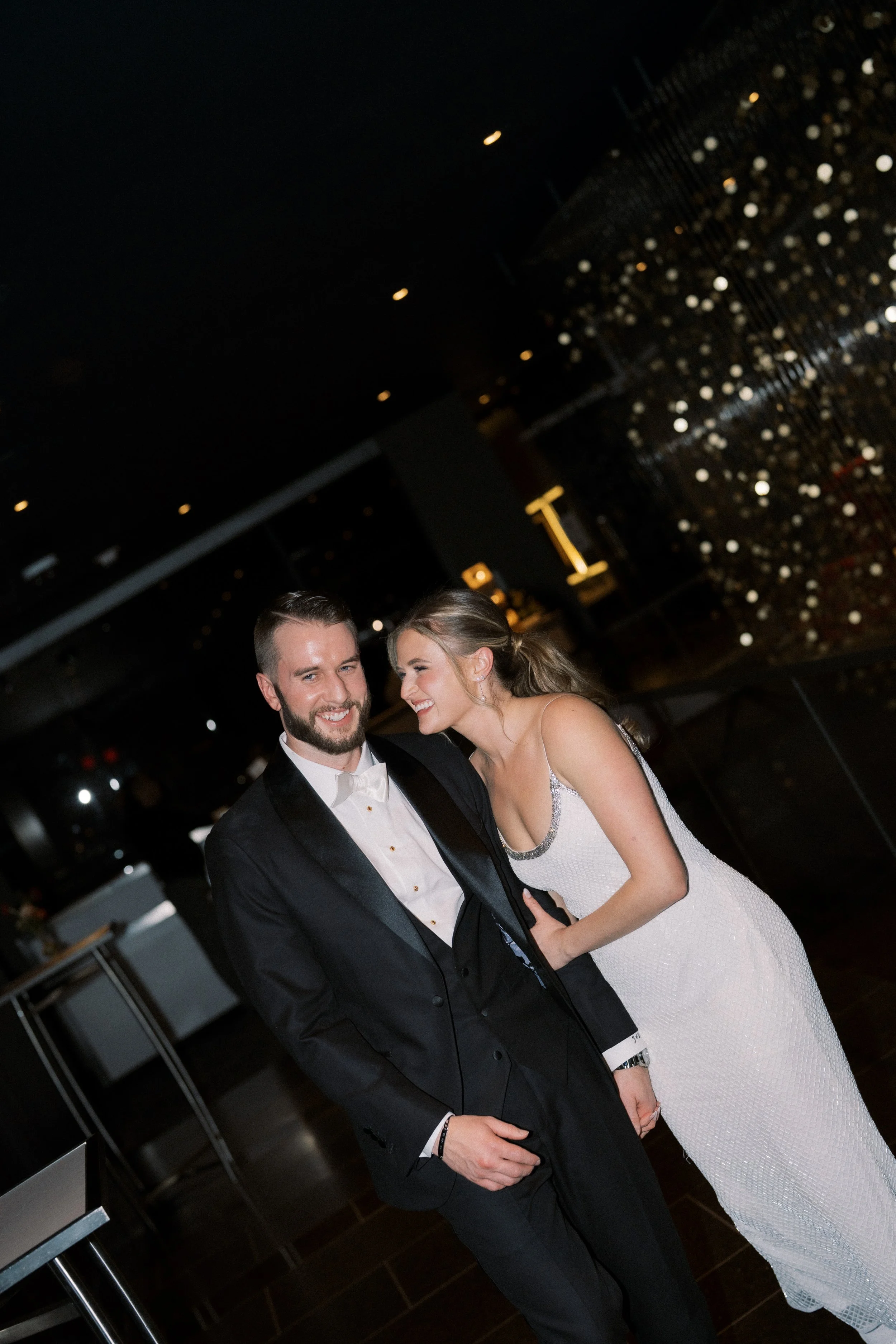 A bride and groom dancing at their wedding reception, smiling and enjoying the moment in an elegant, dimly lit environment.