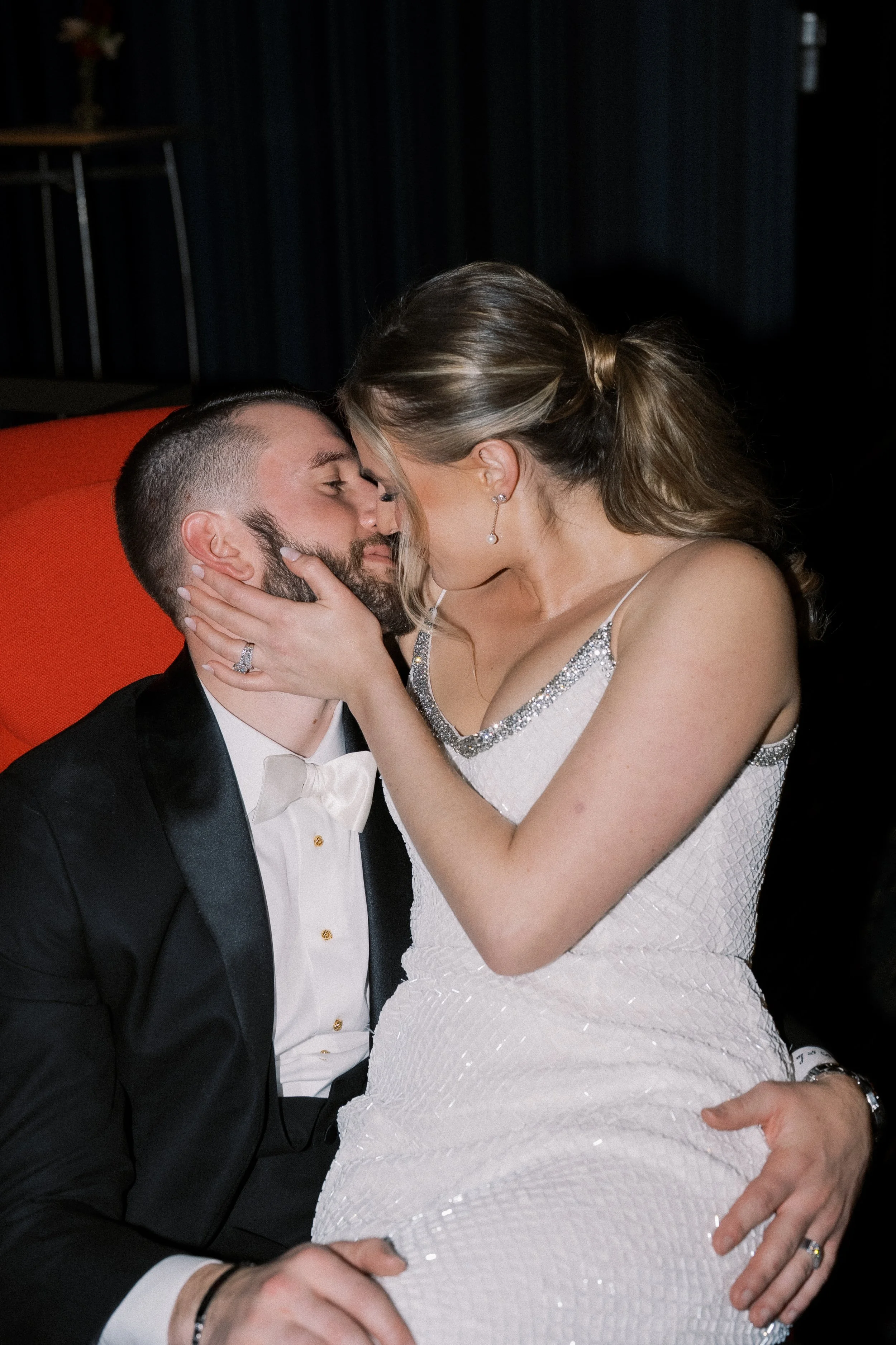 A couple in formal attire sharing a kiss on a black background.