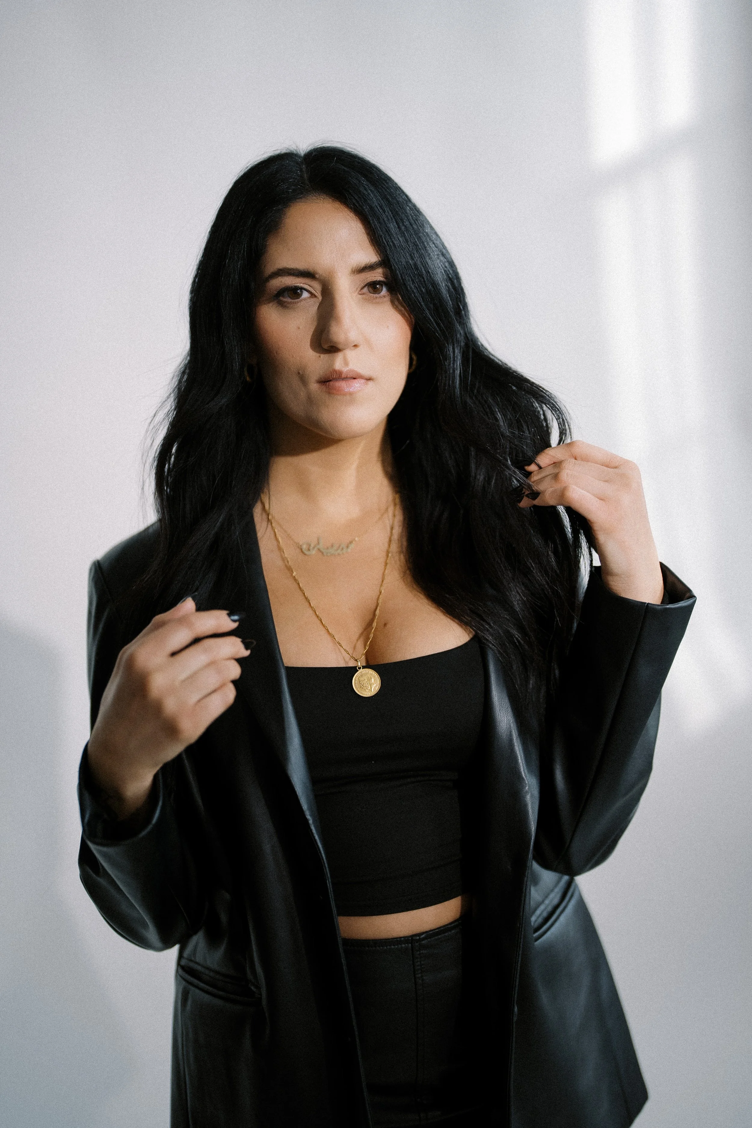 A woman with long black hair and gold jewelry posing indoors.
