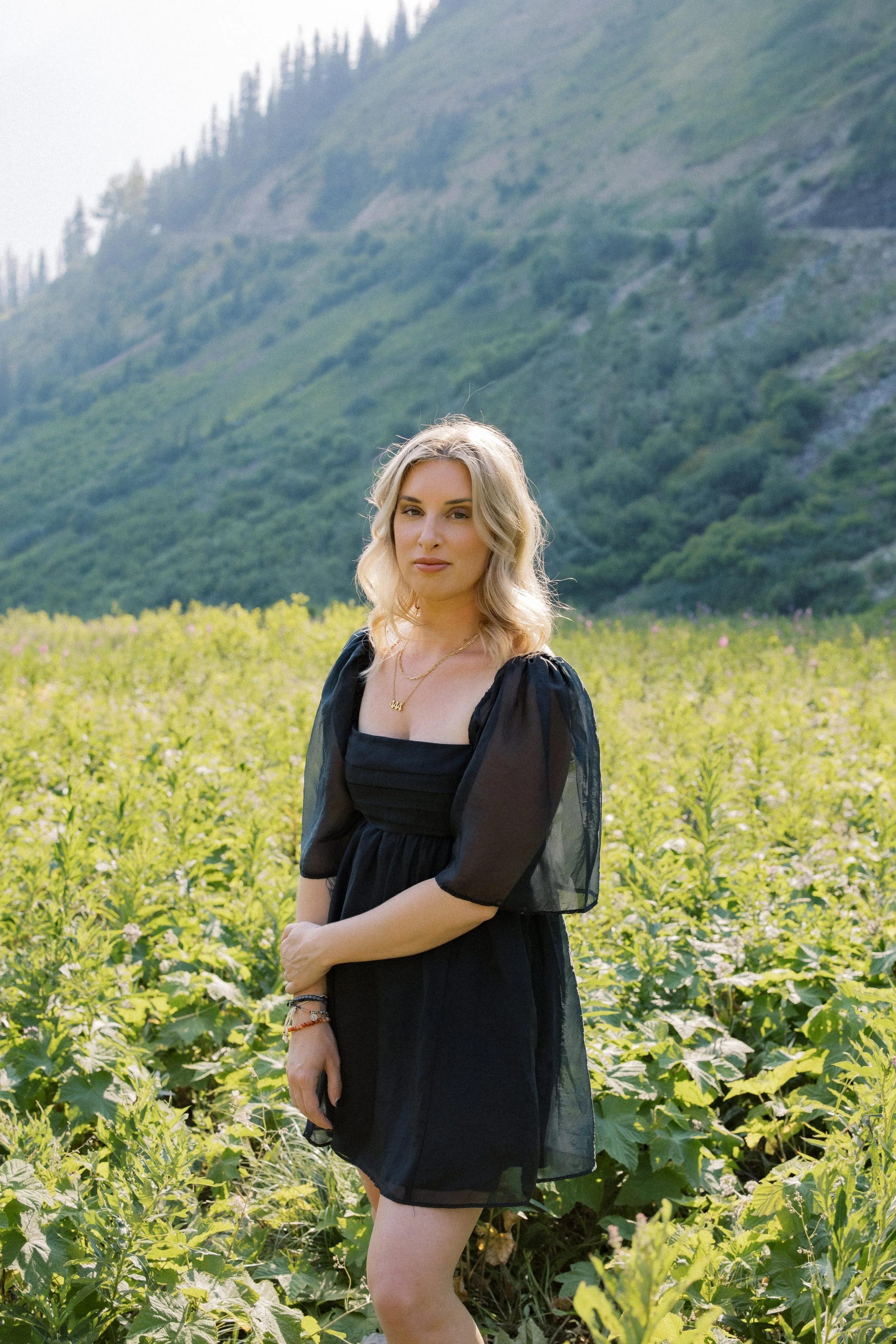 A woman with blonde hair standing in a green field of plants with a mountain background.