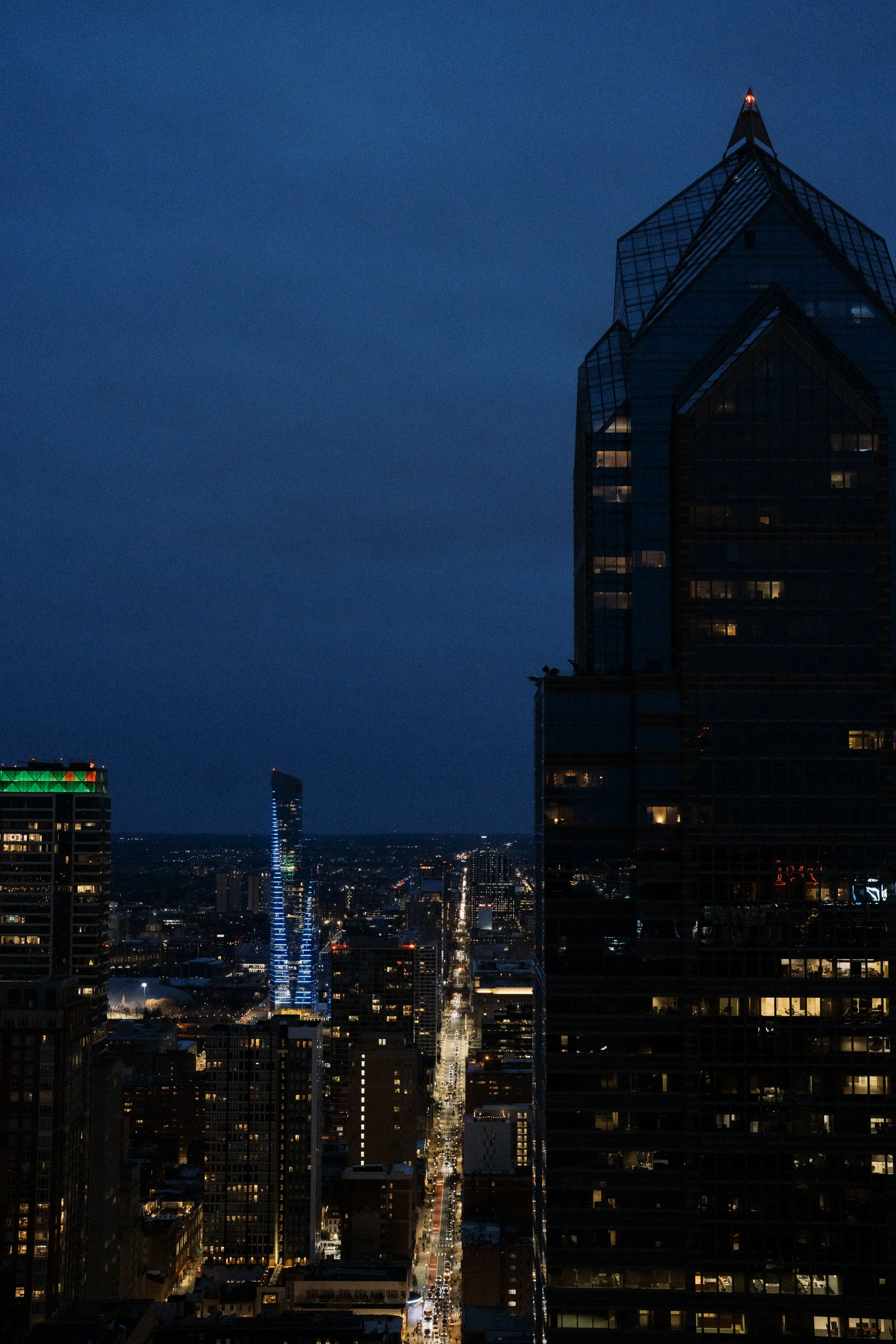 Nighttime cityscape of a downtown area with tall skyscrapers, illuminated streets, and a dark blue sky.