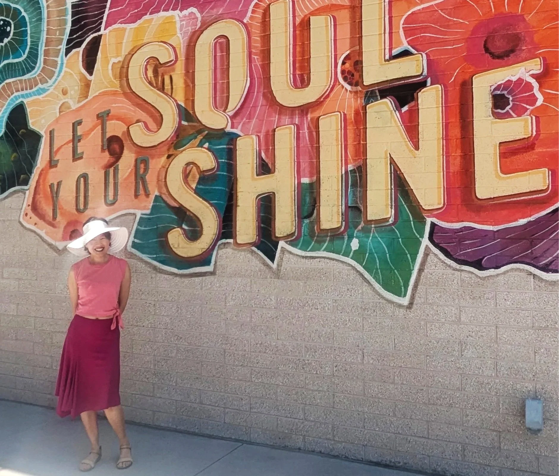 Rosa Phoenix standing in front of a wall mural with the colorful words "Let Your Soul Shine"